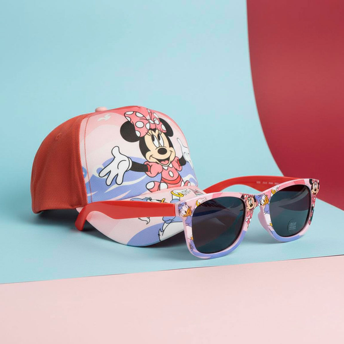 Una gorra rosa de Minnie Mouse y gafas a juego sobre un fondo azul, rosa y rojo.