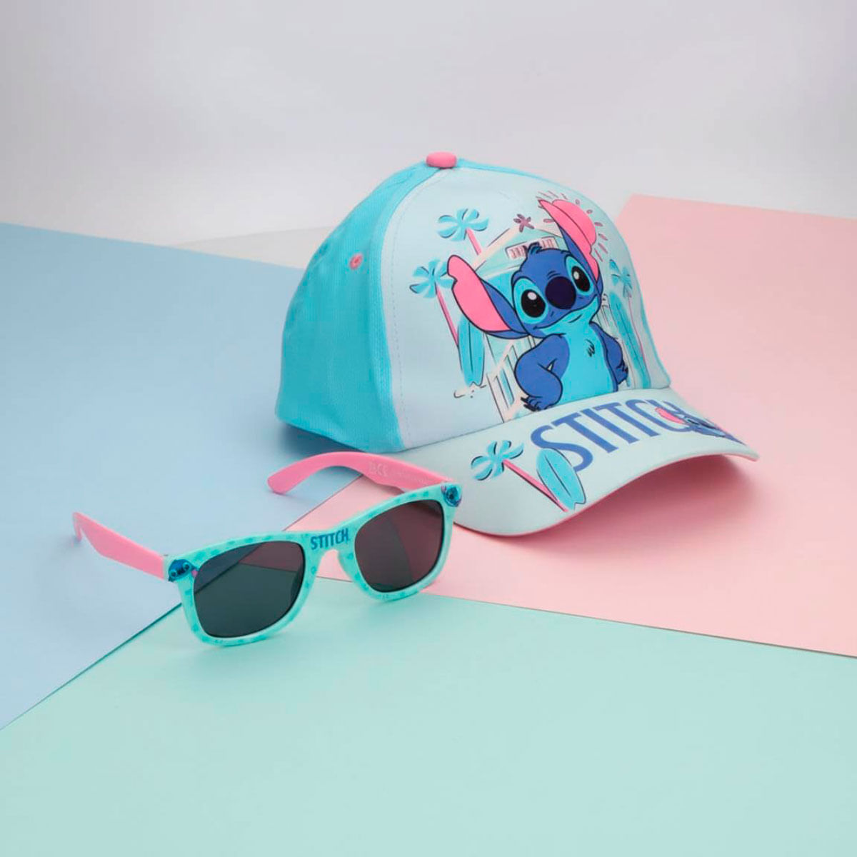 Gorra azul de Stitch y gafas de sol a juego sobre un fondo rosa y azul claro.