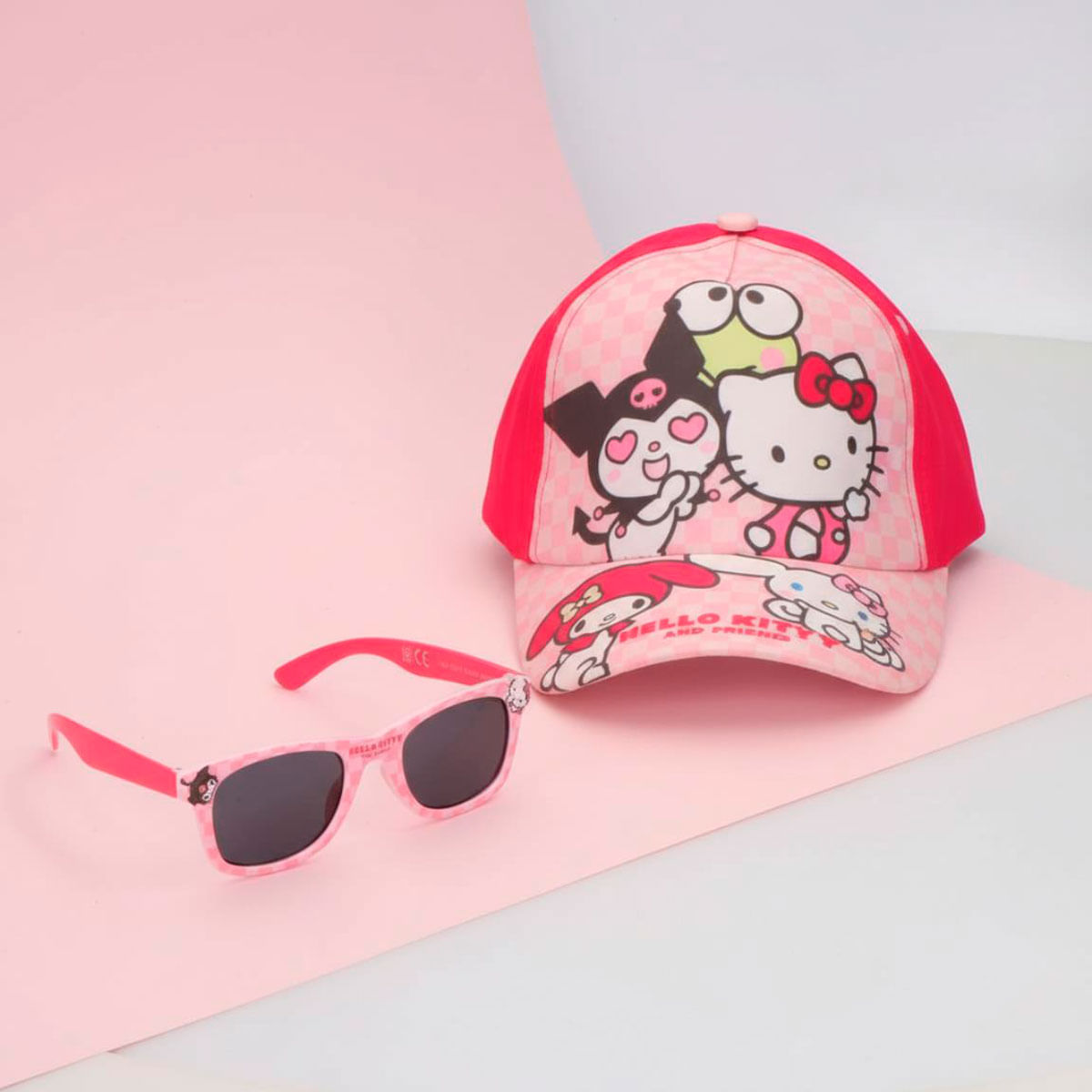 Gorra de béisbol rosa de Hello Kitty y gafas de sol a juego sobre un fondo rosa y blanco.