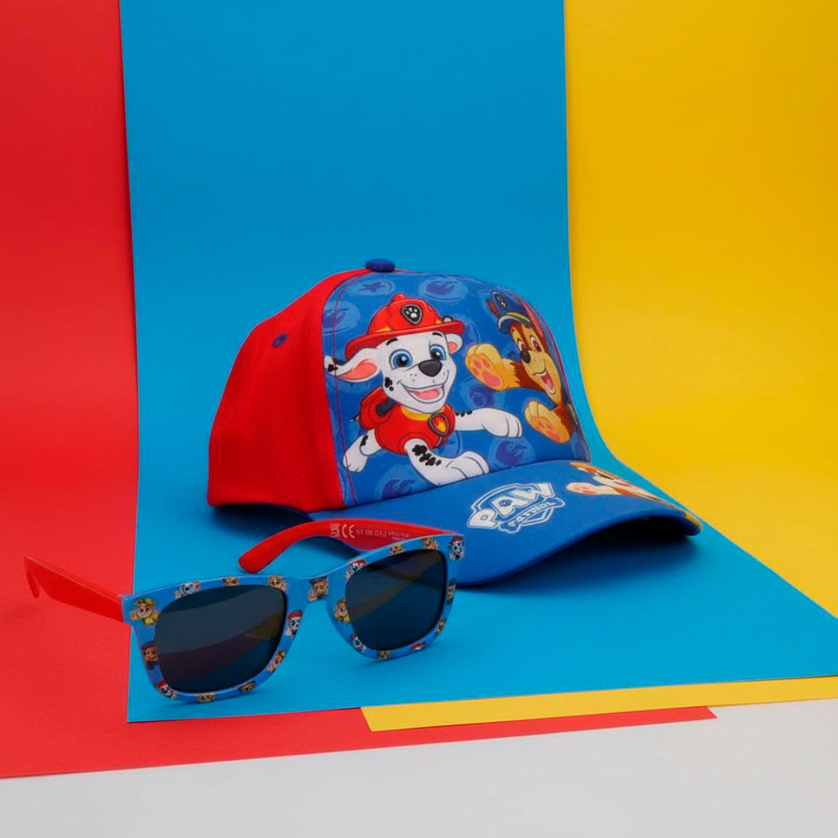 Gorra azul y roja de Paw Patrol con gafas de sol a juego sobre un fondo colorido.