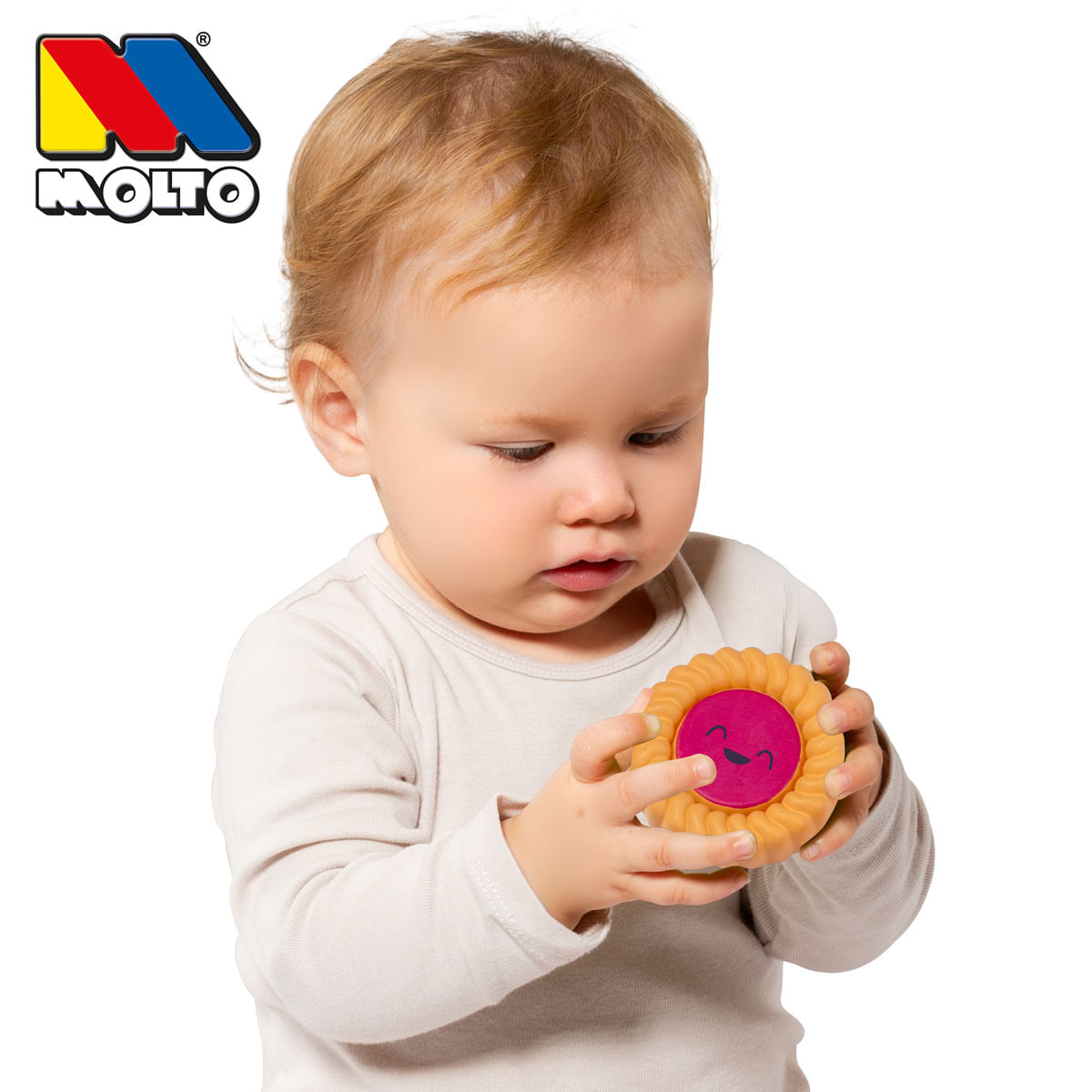 Un niño pequeño sostiene un juguete de galleta redondo y sonriente con centro rosa sobre fondo blanco.
