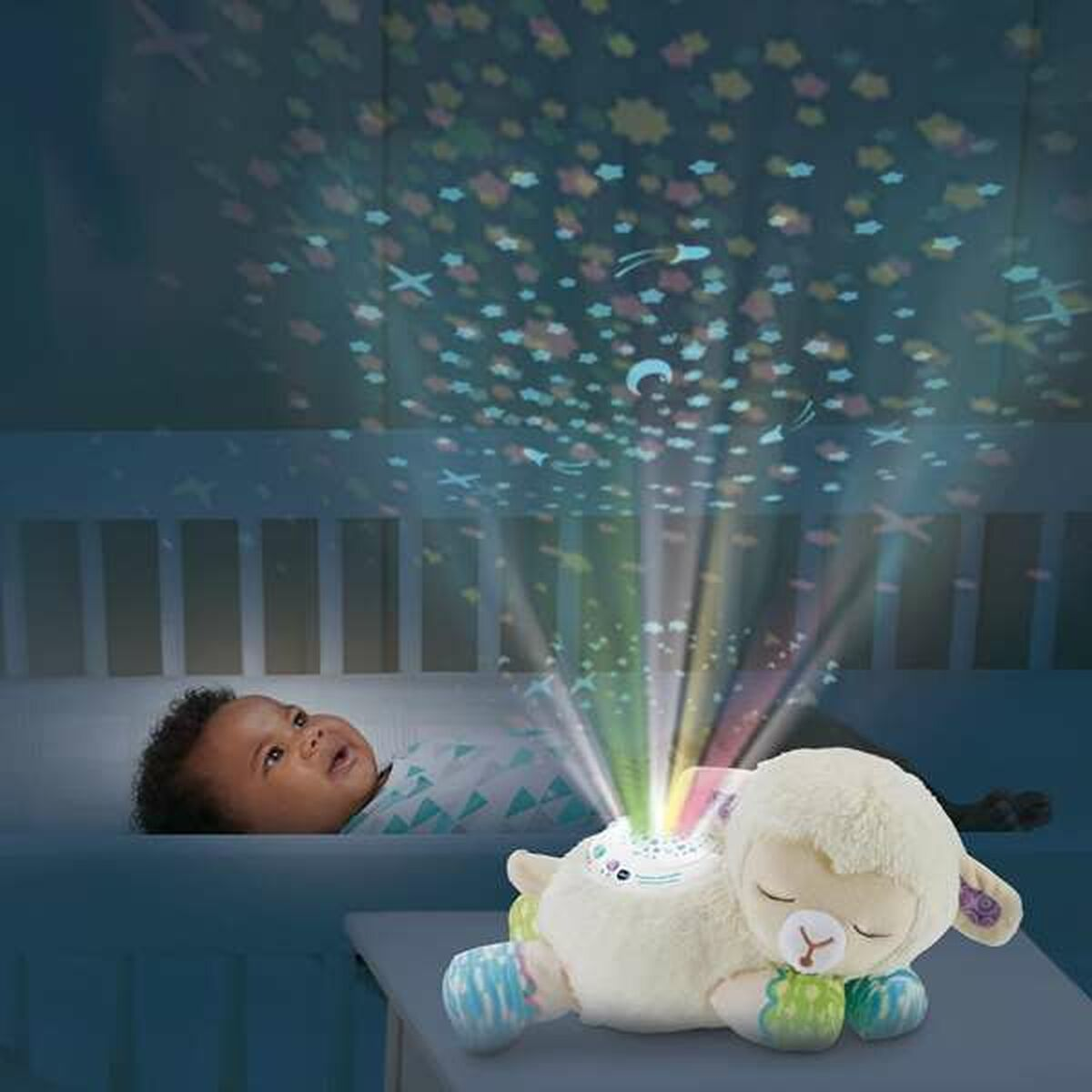 Un proyector de oveja de peluche proyecta estrellas coloridas en el techo mientras un bebé observa desde la cama.