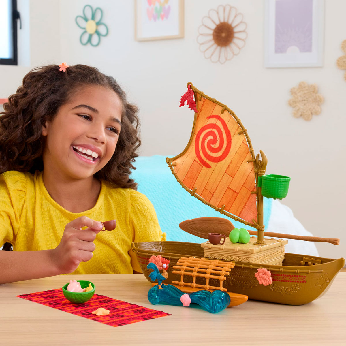 Una niña sonriente con camisa amarilla juega con un barco de juguete y figuras.