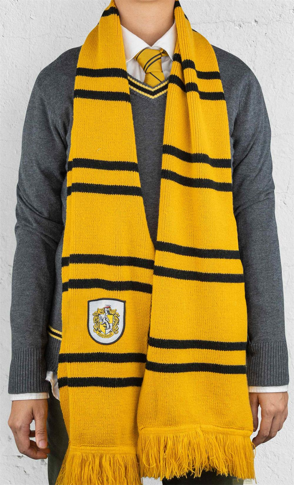 Une personne porte un pull gris, une écharpe jaune et noire avec écusson et cravate sur fond blanc.