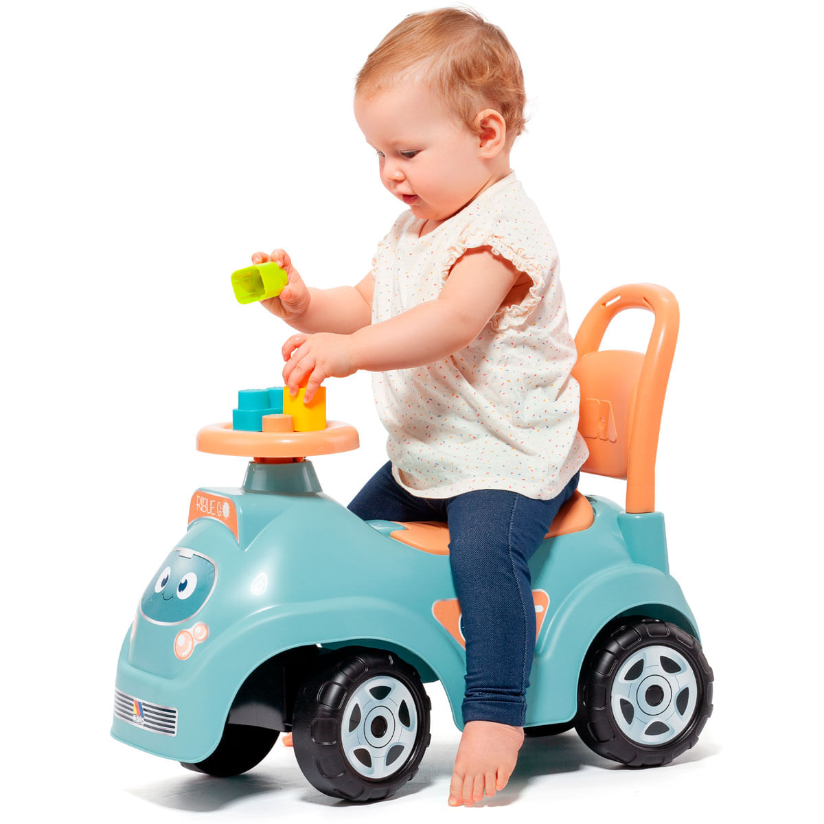 Niño pequeño sentado en un coche de juguete azul jugando con bloques de colores.