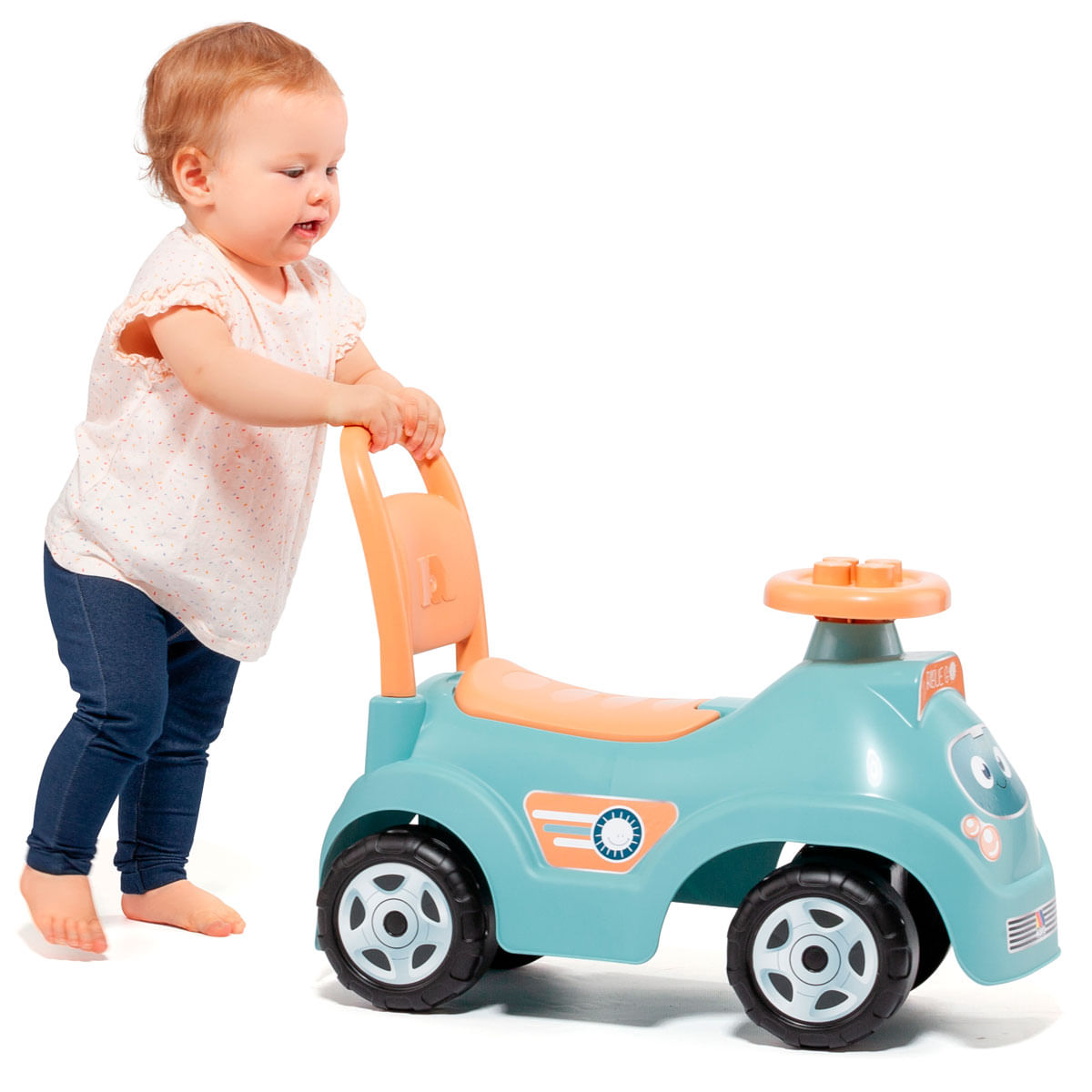 Niño pequeño empuja un coche de juguete azul claro con asiento y volante naranjas sobre fondo blanco.