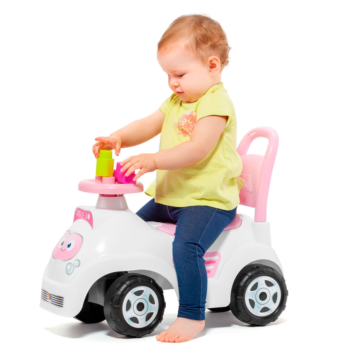 Niño pequeño sentado en un auto de juguete blanco y rosa jugando con bloques.