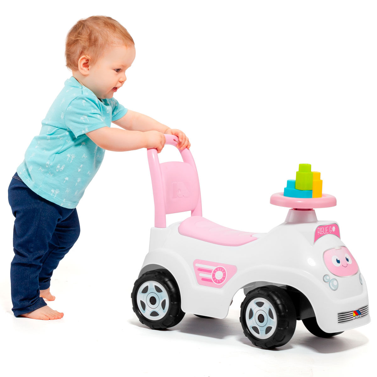 Niño pequeño con camiseta azul empuja un auto de juguete blanco y rosa con bloques coloridos.
