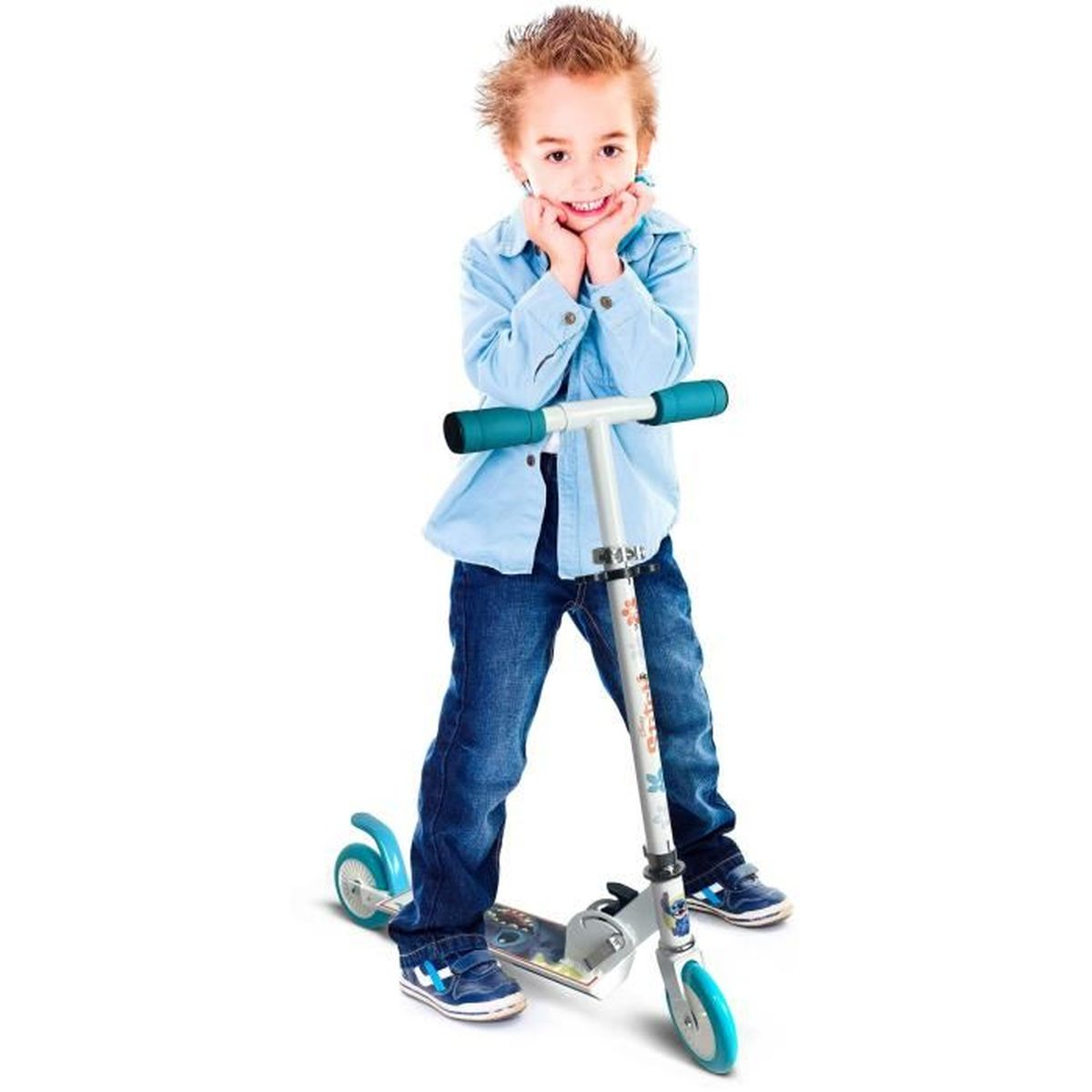 Un niño sonriente con camisa azul clara y vaqueros está de pie con las manos en la cara detrás de un patinete blanco y azul.