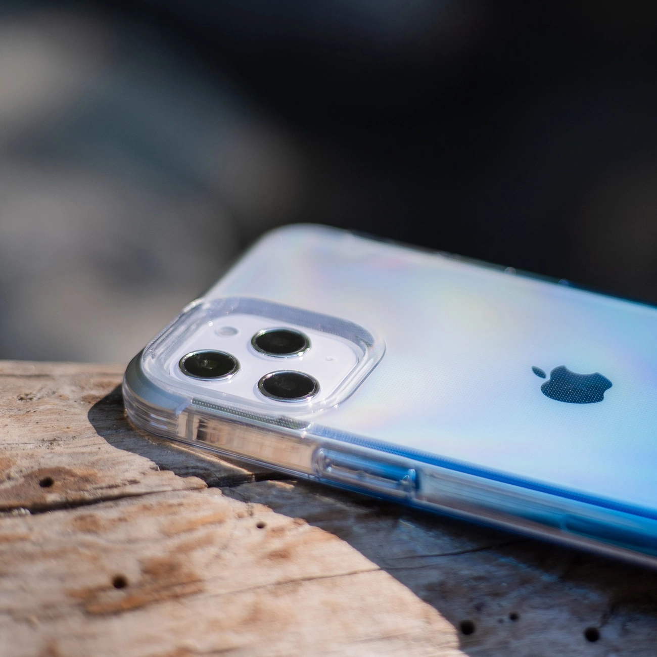 Uno smartphone in una cover trasparente su una superficie di legno ruvida, focalizzato sulla tripla fotocamera.