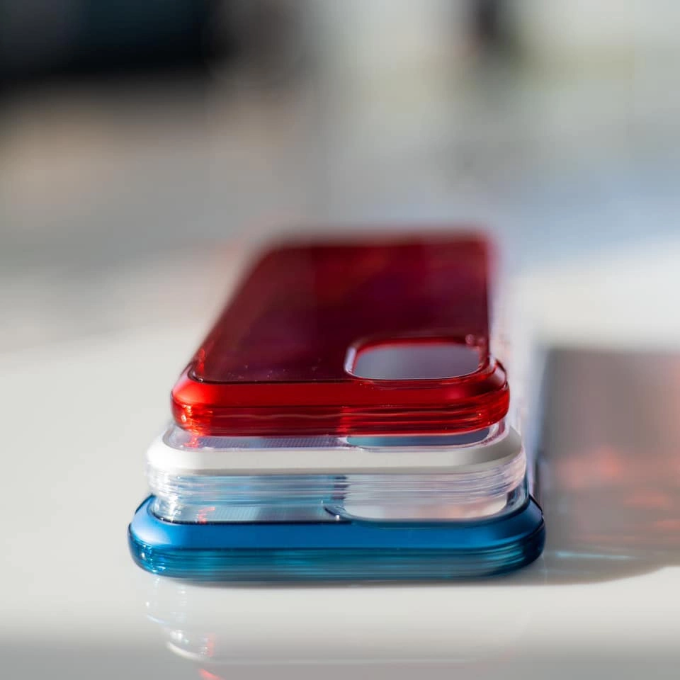 Una pila di tre custodie lucide per cellulari nei colori rosso, bianco e blu su una superficie bianca riflettente.