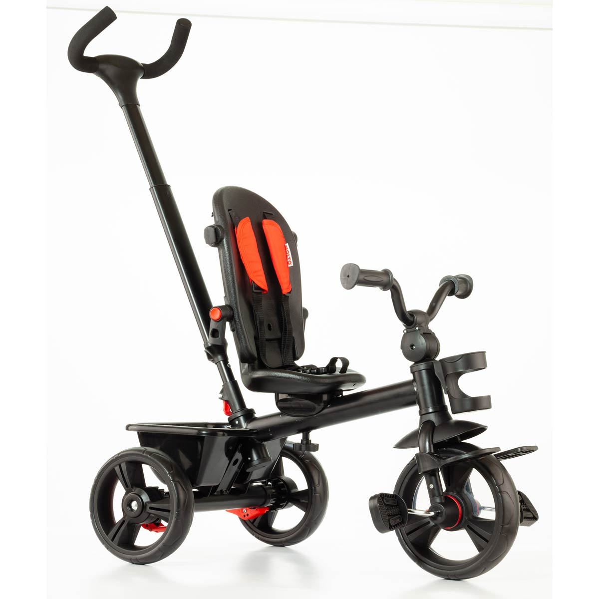 Un triciclo negro para niños pequeños con barra de empuje, cesta de almacenamiento, cojines rojos y fondo blanco.