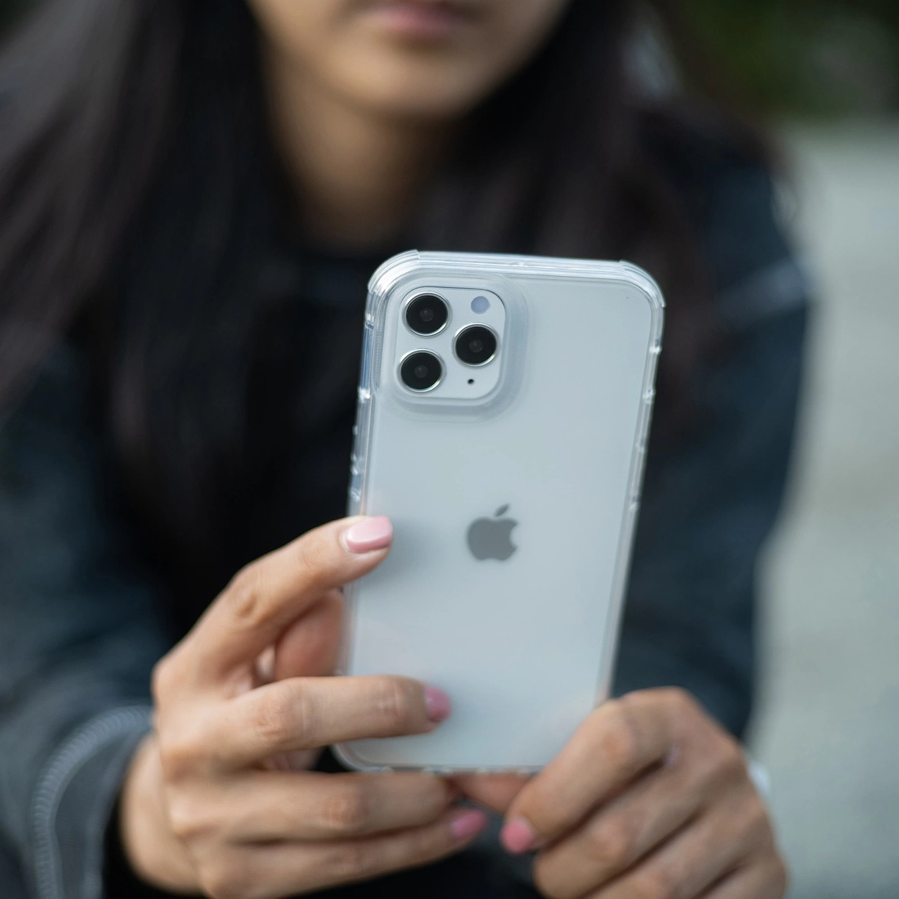 Una persona tiene in mano uno smartphone bianco con cover trasparente e tripla fotocamera.