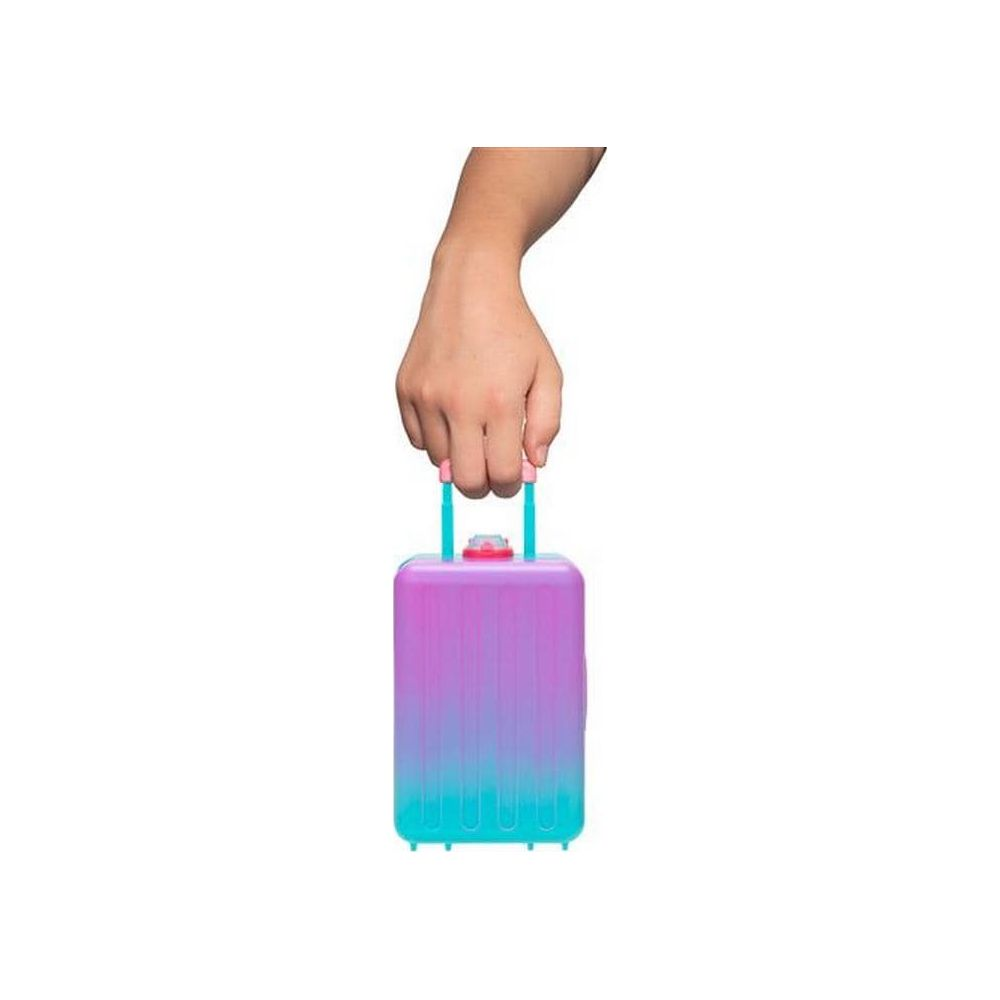 Una mano sostiene una pequeña maleta de juguete con degradado rosa y azul por su asa sobre fondo blanco.