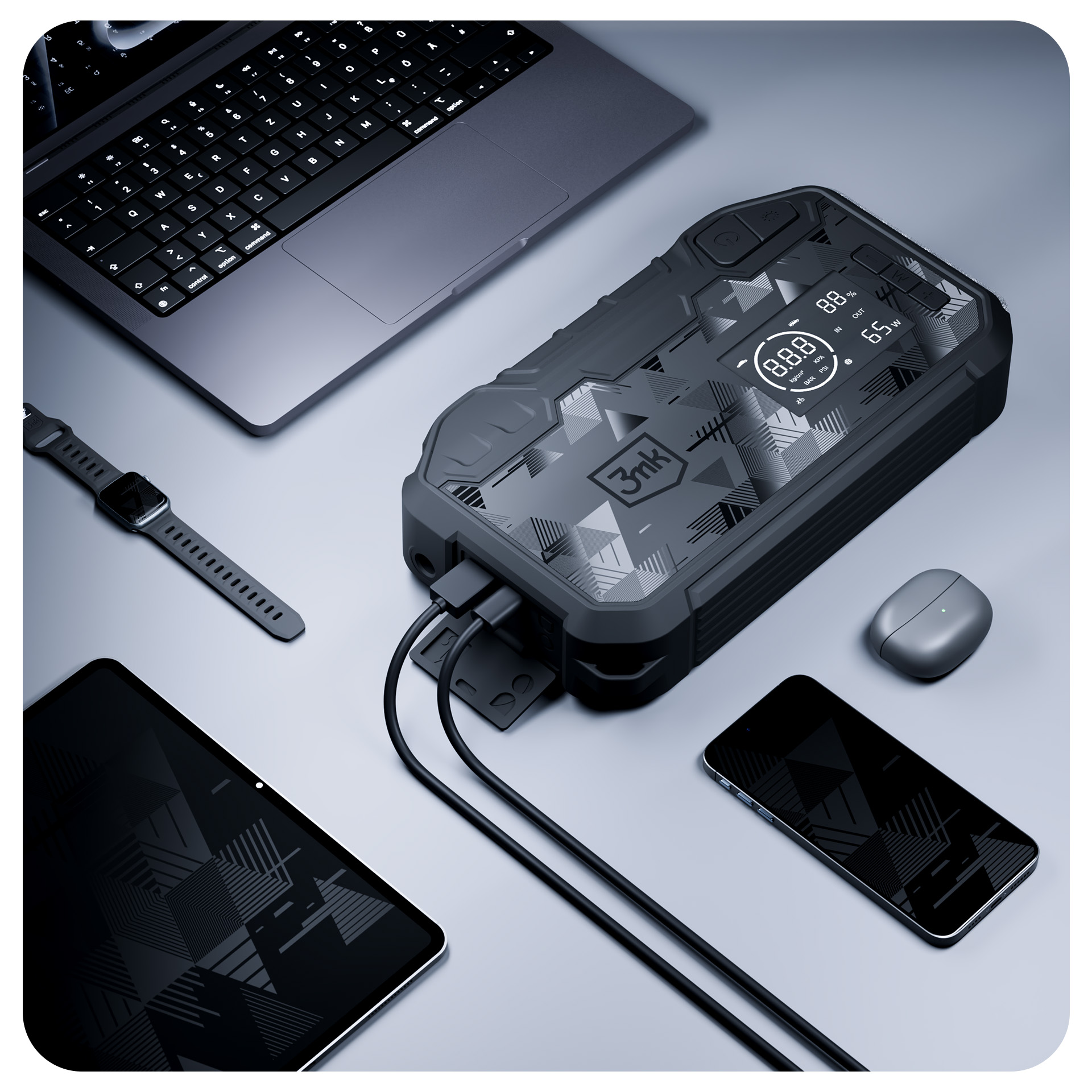 Czarny powerbank z cyfrowym wyświetlaczem na stole obok laptopa, tabletu, smartfona i słuchawek.