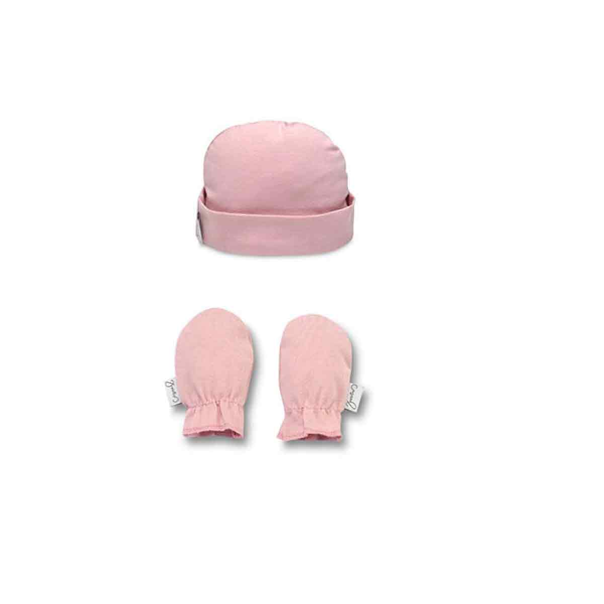 Un gorrito de bebé rosa y un par de manoplas a juego sobre un fondo blanco.