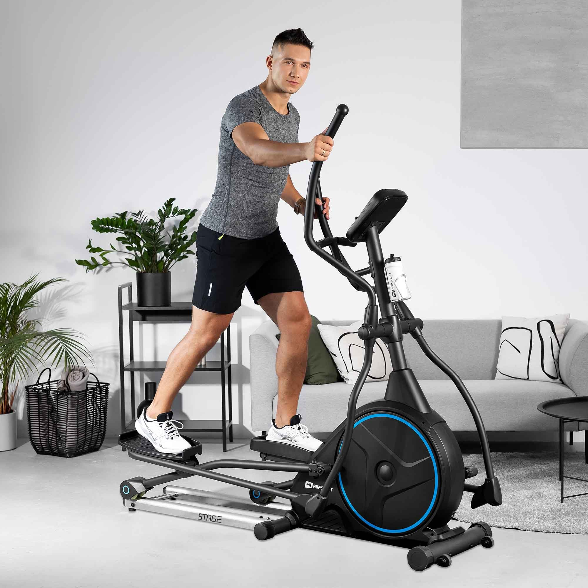 Ein Mann trainiert auf einem Heimtrainer in einem modernen Wohnzimmer mit Pflanzen und Sofa.