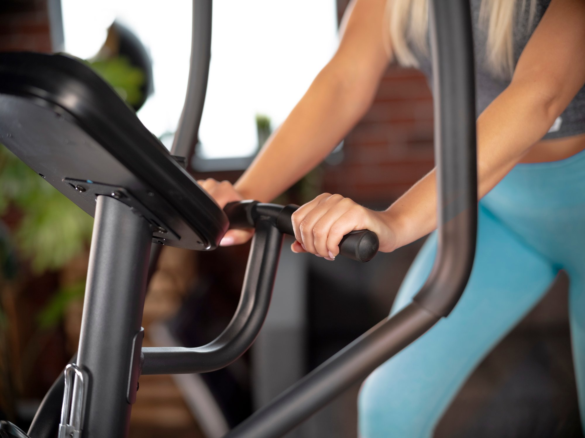 Eine blonde Frau in blauen Leggings trainiert auf einem Heimtrainer in einem Fitnessstudio.