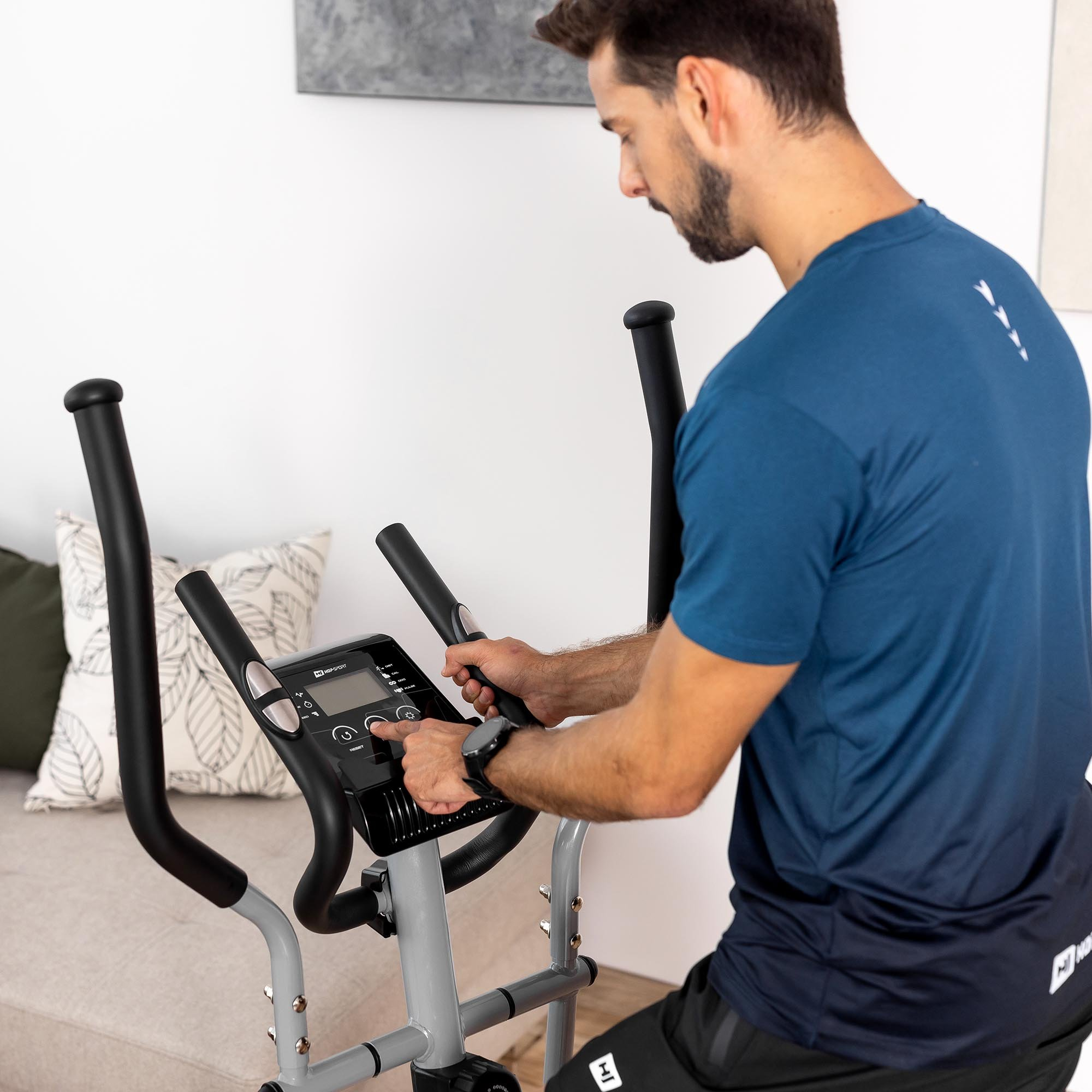 Ein Mann in einem blauen T-Shirt stellt den Computer eines Crosstrainers ein.