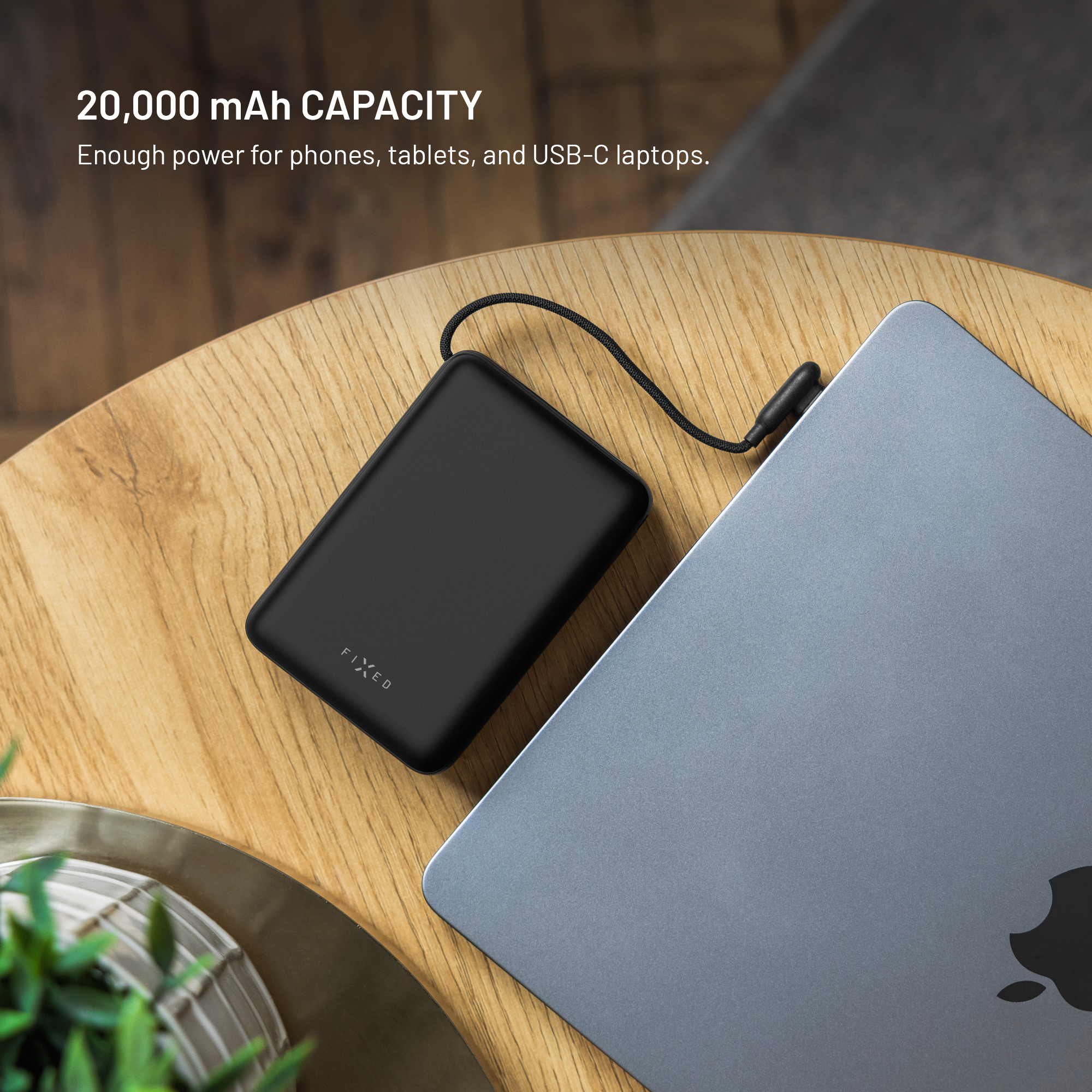 Eine schwarze Powerbank liegt neben einem Laptop auf einem Holztisch.