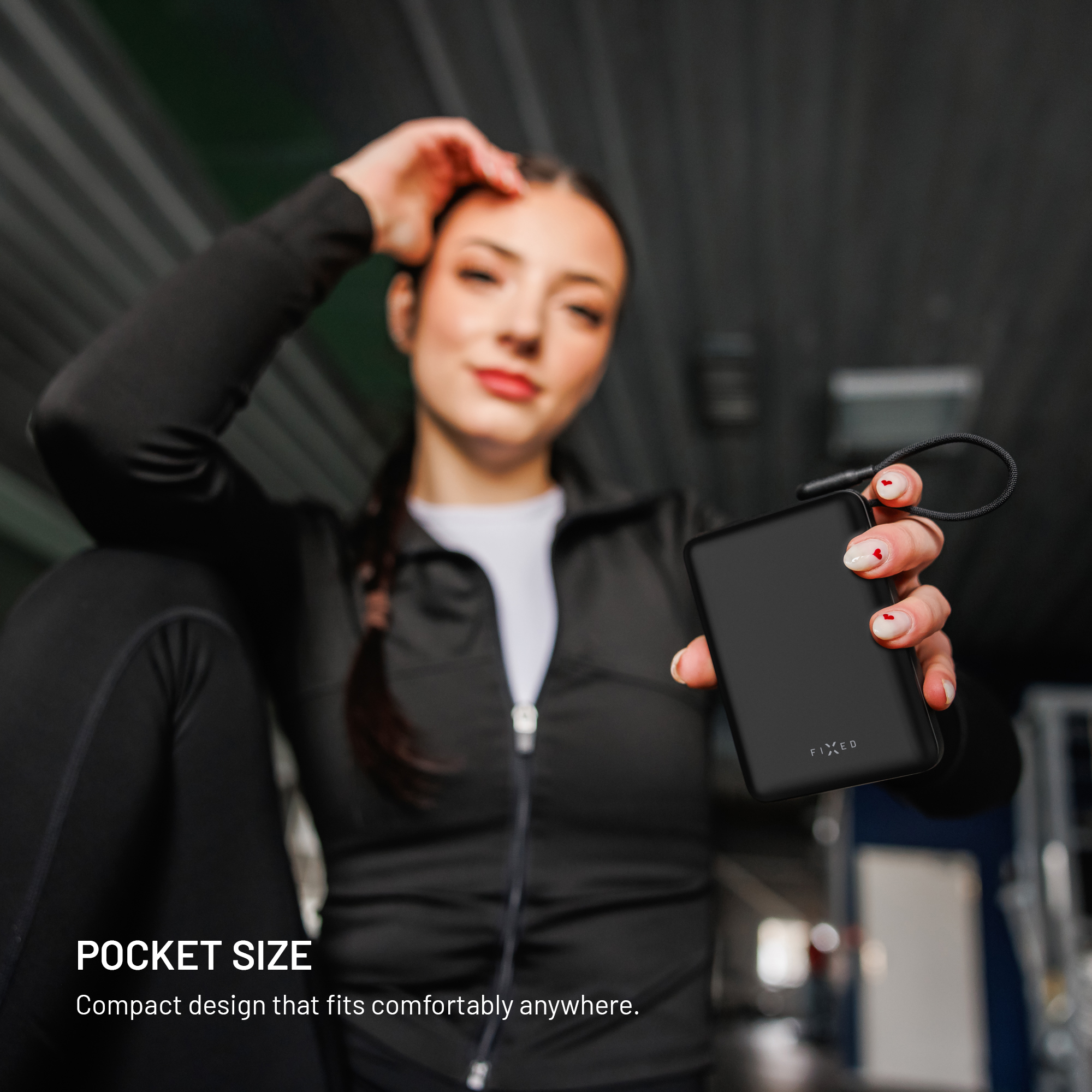 Eine Frau in Sportkleidung hält eine kleine schwarze Powerbank in die Kamera.