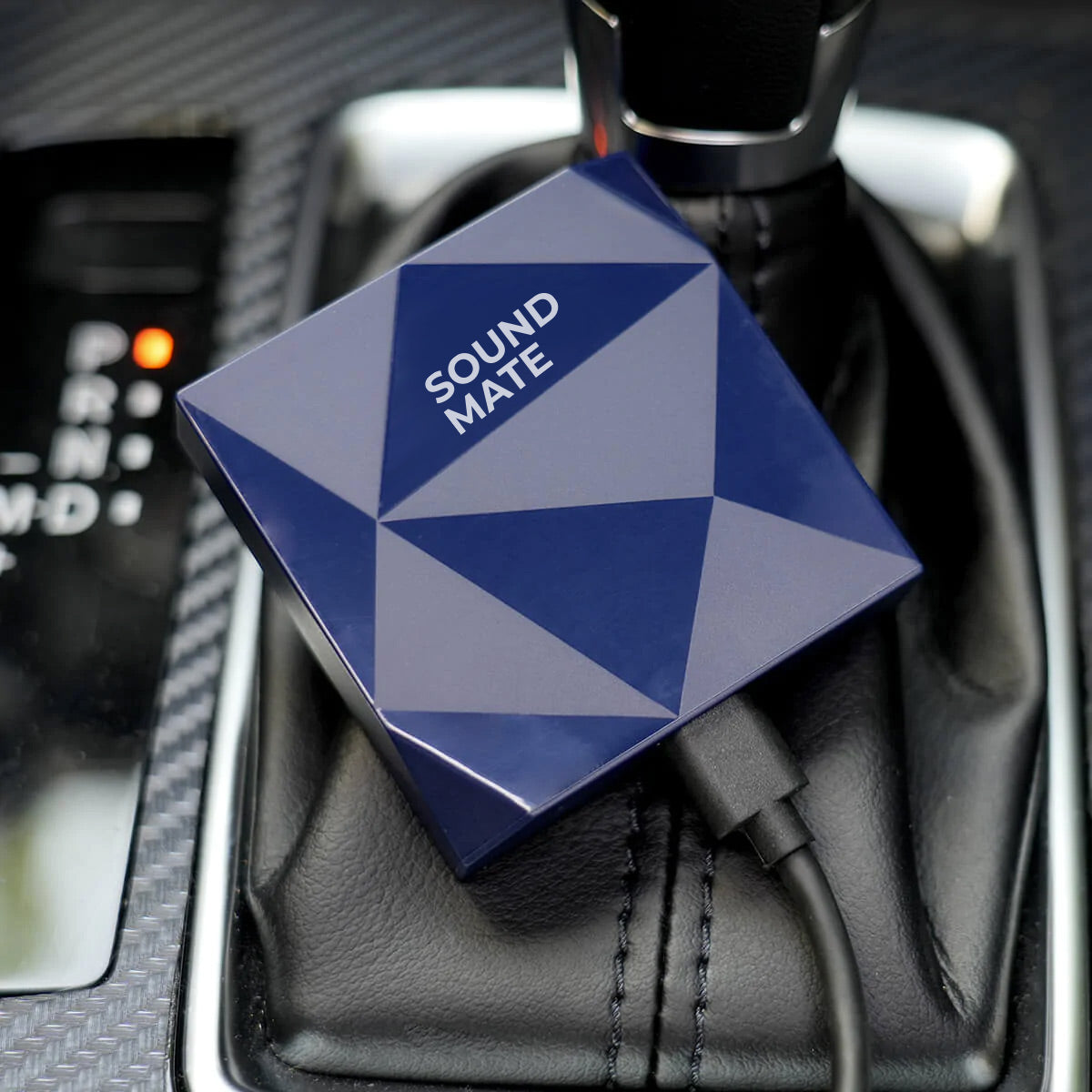Ein blaues Sound Mate-Gerät mit geometrischem Muster ist in der Mittelkonsole eines Autos in der Nähe der Schaltung eingesteckt.