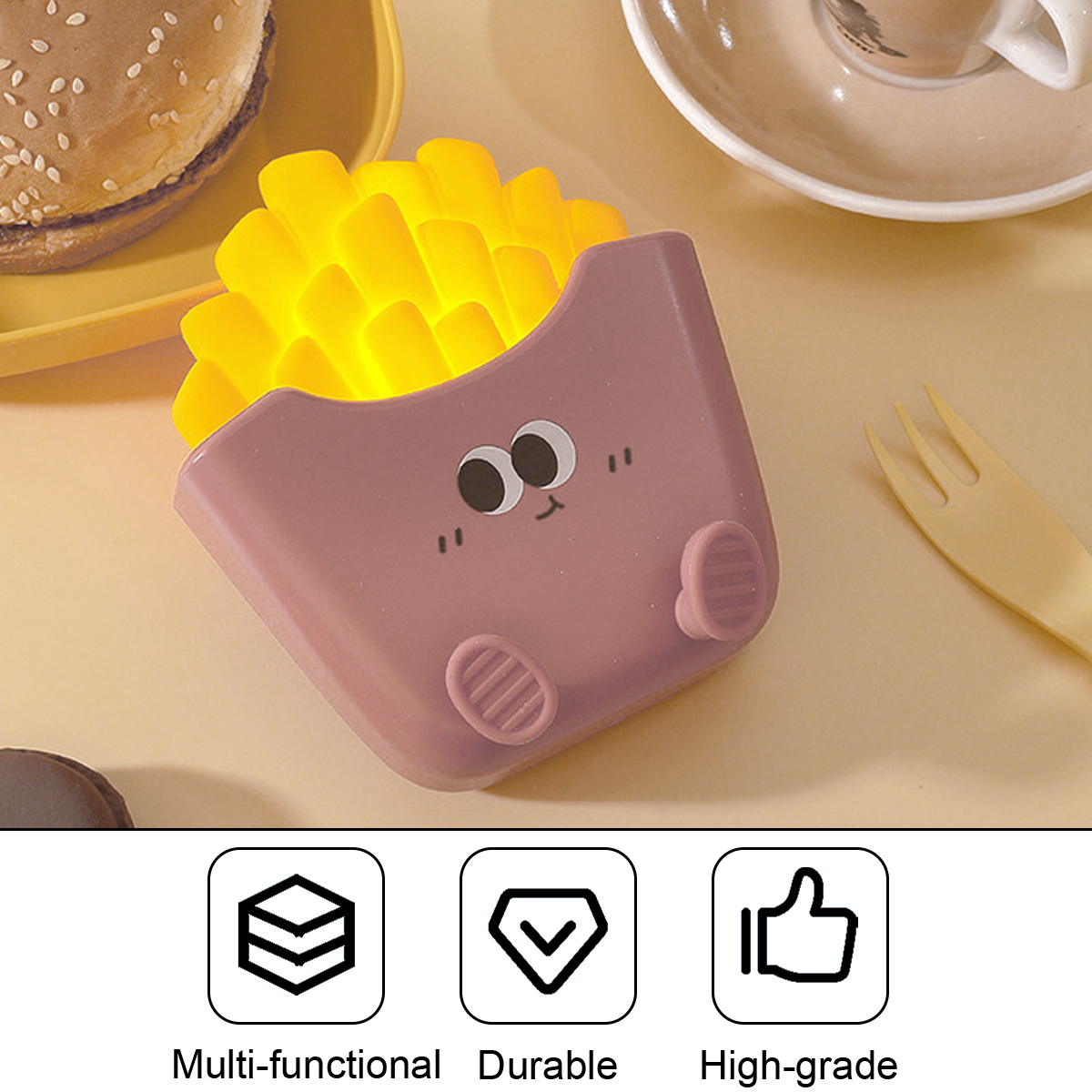 Eine rosafarbene Pommes-Nachtlampe mit Gesicht sitzt auf einem Tisch neben einem Burger und einer Kaffeetasse.