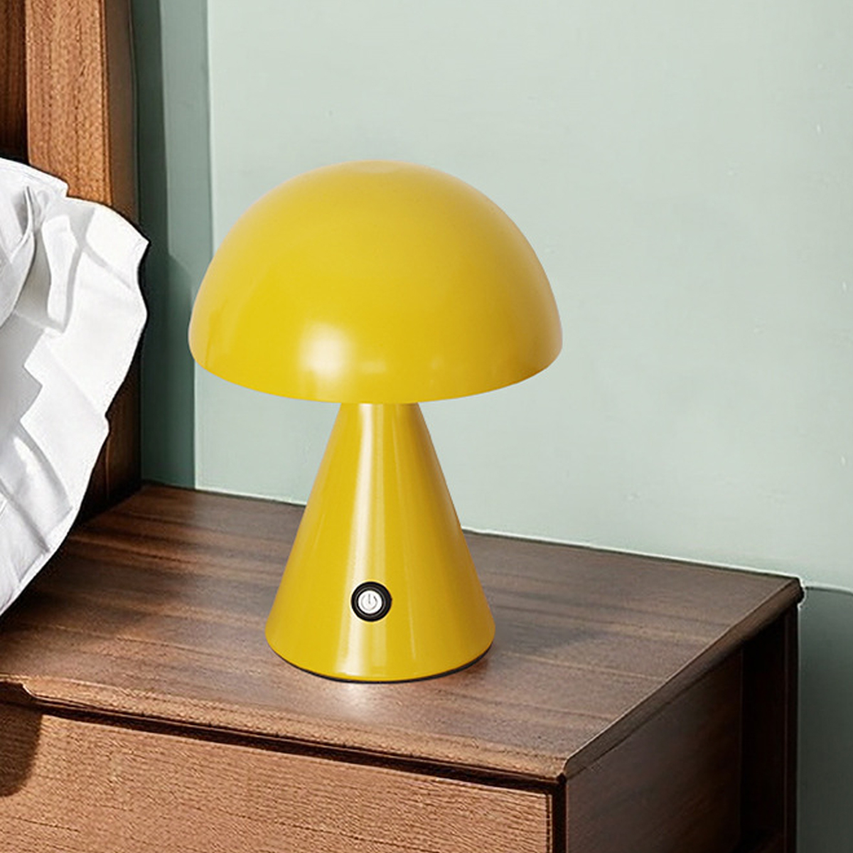 Eine glänzende gelbe Pilzlampe steht auf einem dunklen Holznachttisch vor einer hellgrünen Wand.