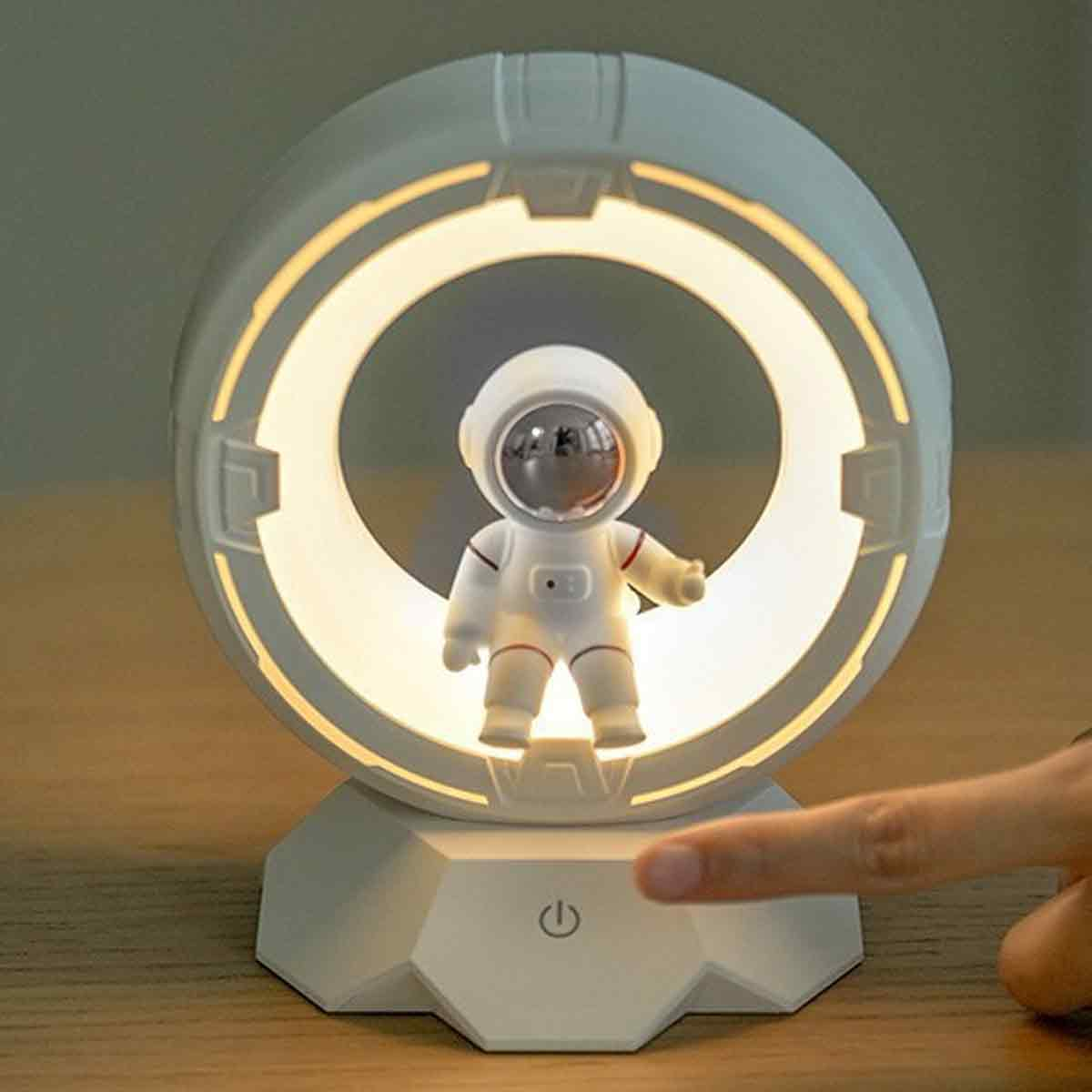 Eine weiße Astronautenlampe mit leuchtendem Ring steht auf einem Tisch, eine Hand berührt den Touch-Schalter.