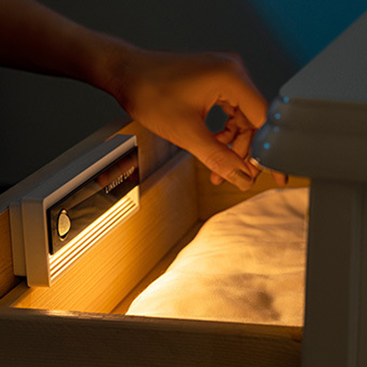 Eine Hand öffnet eine Schublade, die von einem warmen LED-Streifen beleuchtet wird.