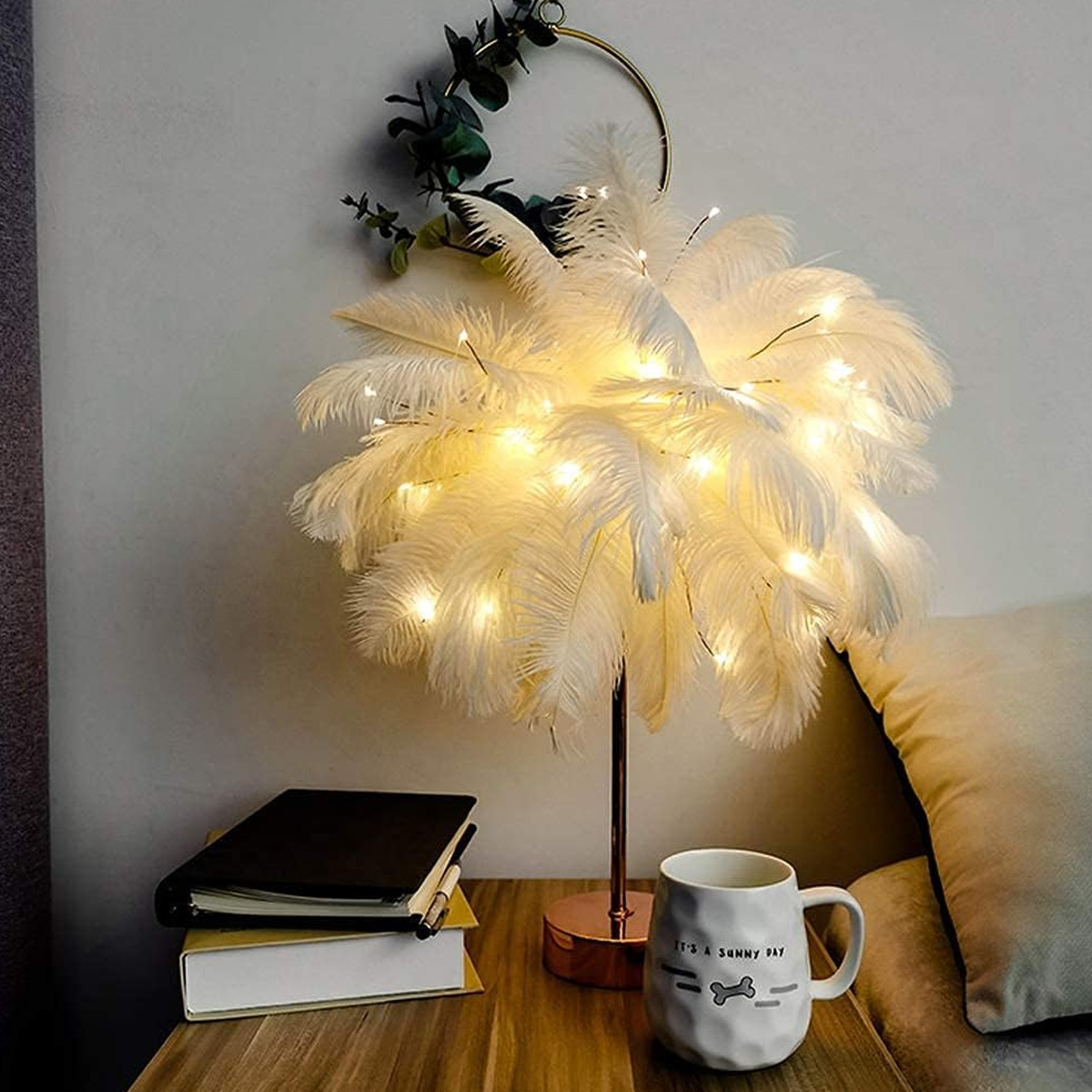 Eine flauschige weiße Federlampe mit warmen Lichterketten steht auf einem Nachttisch.