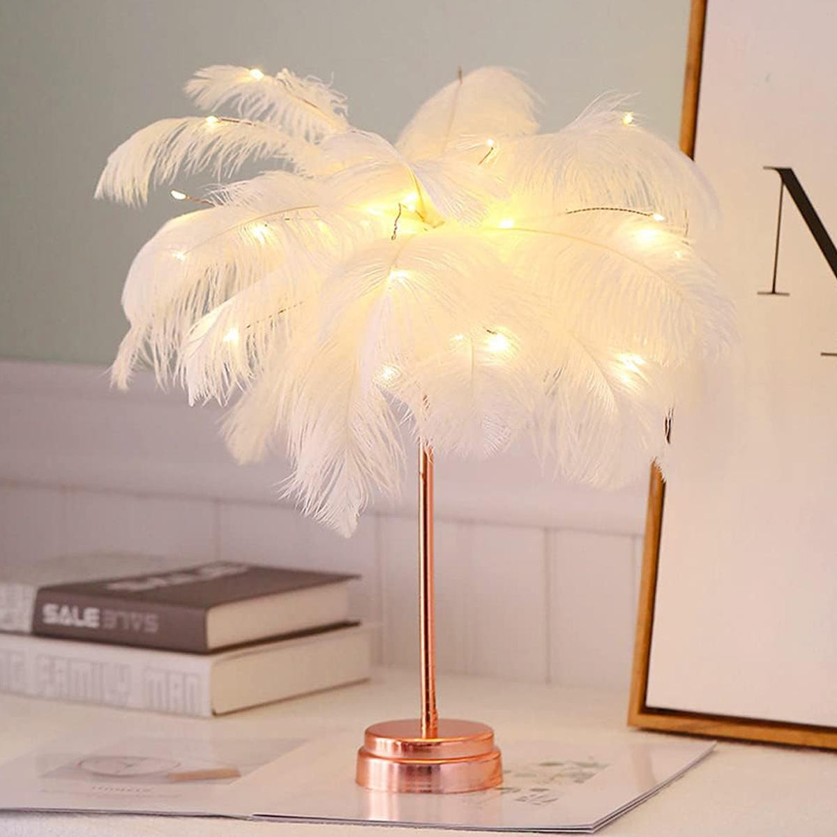Eine elegante Tischlampe mit weißen Federn und warmen LED-Lichtern auf einem roségoldenen Ständer.