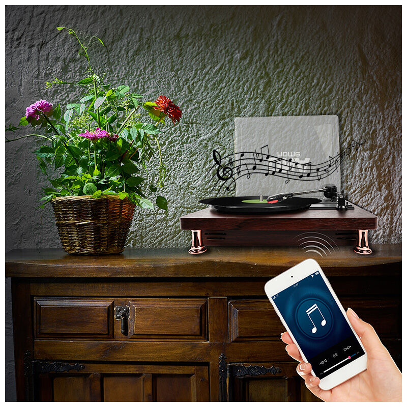 Ein Plattenspieler steht auf einem Holzschrank neben einer Pflanze, während ein Smartphone Musik abspielt.