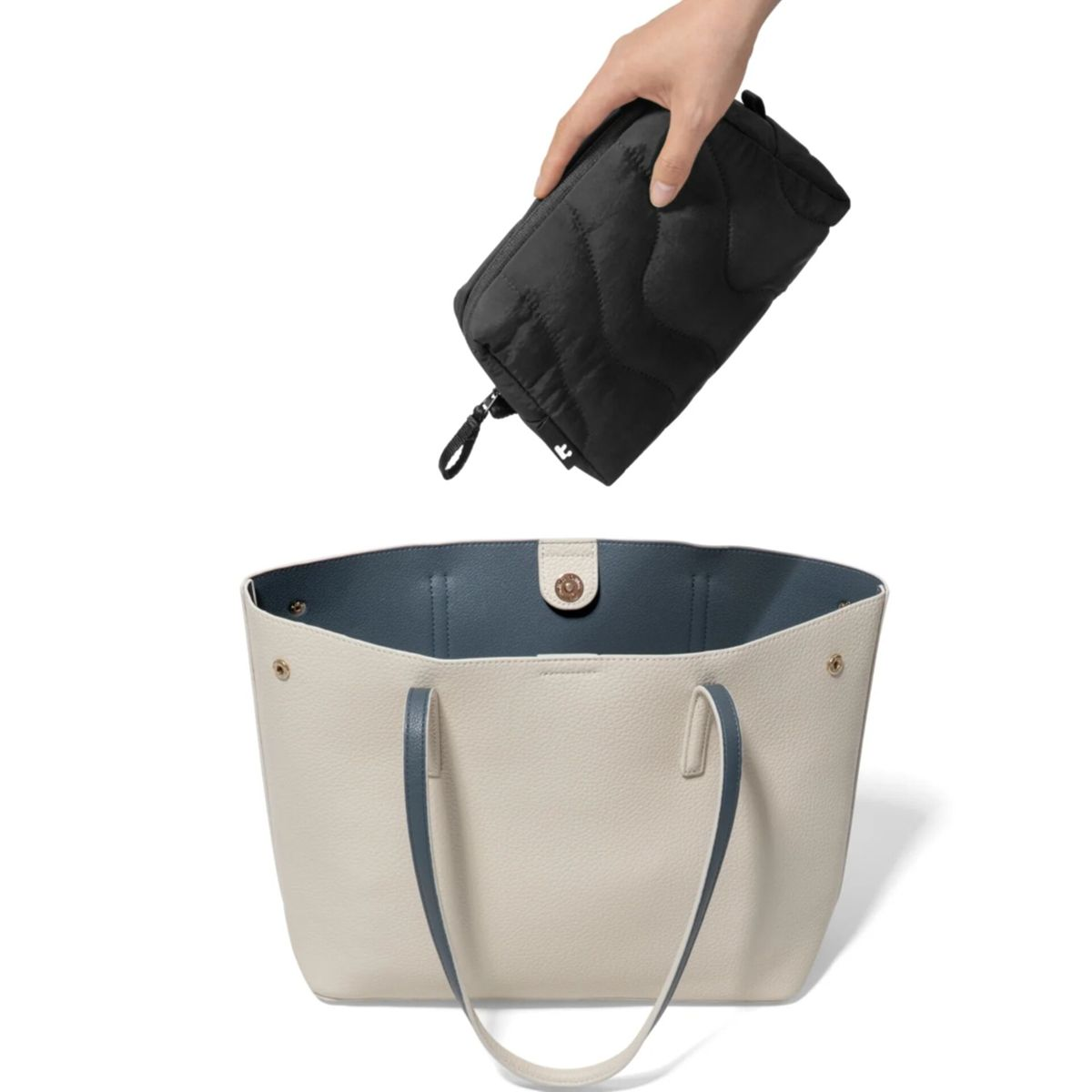 Eine Hand legt eine schwarze Tasche in einen cremefarbenen Shopper.