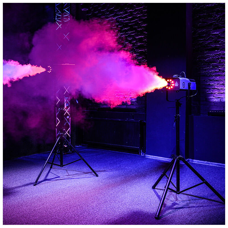 Eine Nebelmaschine auf einem Stativ stößt in einem Raum mit dunklem Backstein und violettem Licht dichten Rauch aus.