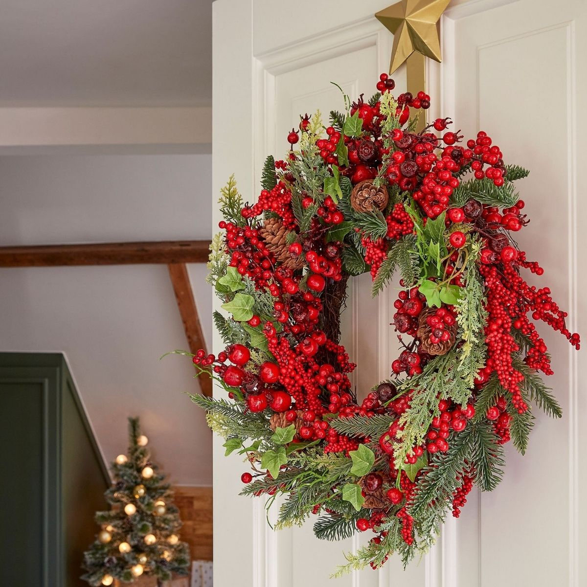 Une couronne de Noël luxuriante avec des baies rouges, des pommes de pin et du feuillage vert accrochée à une porte blanche.