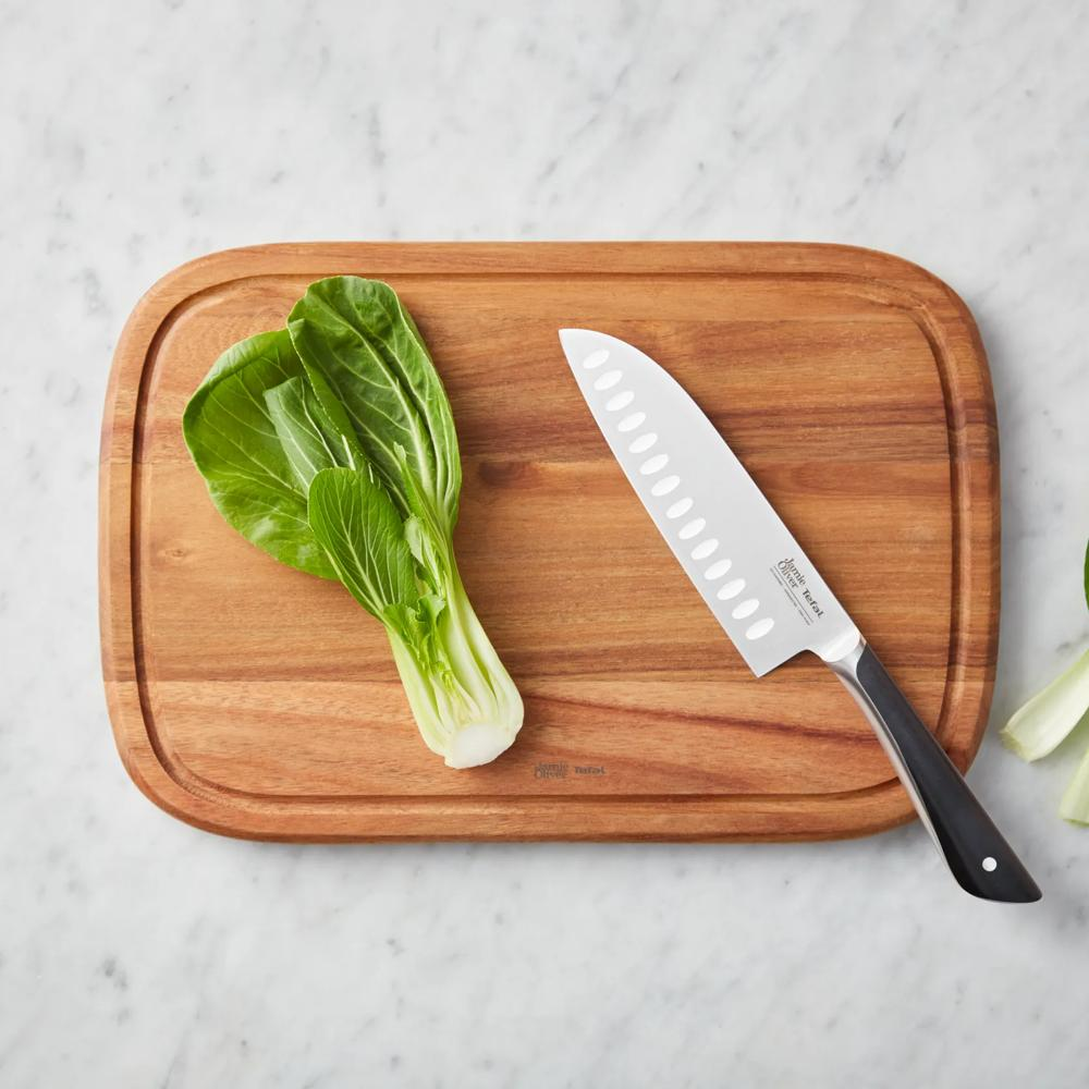 Nóż santoku i świeża kapusta pak choi leżą na drewnianej desce do krojenia na marmurowym blacie.