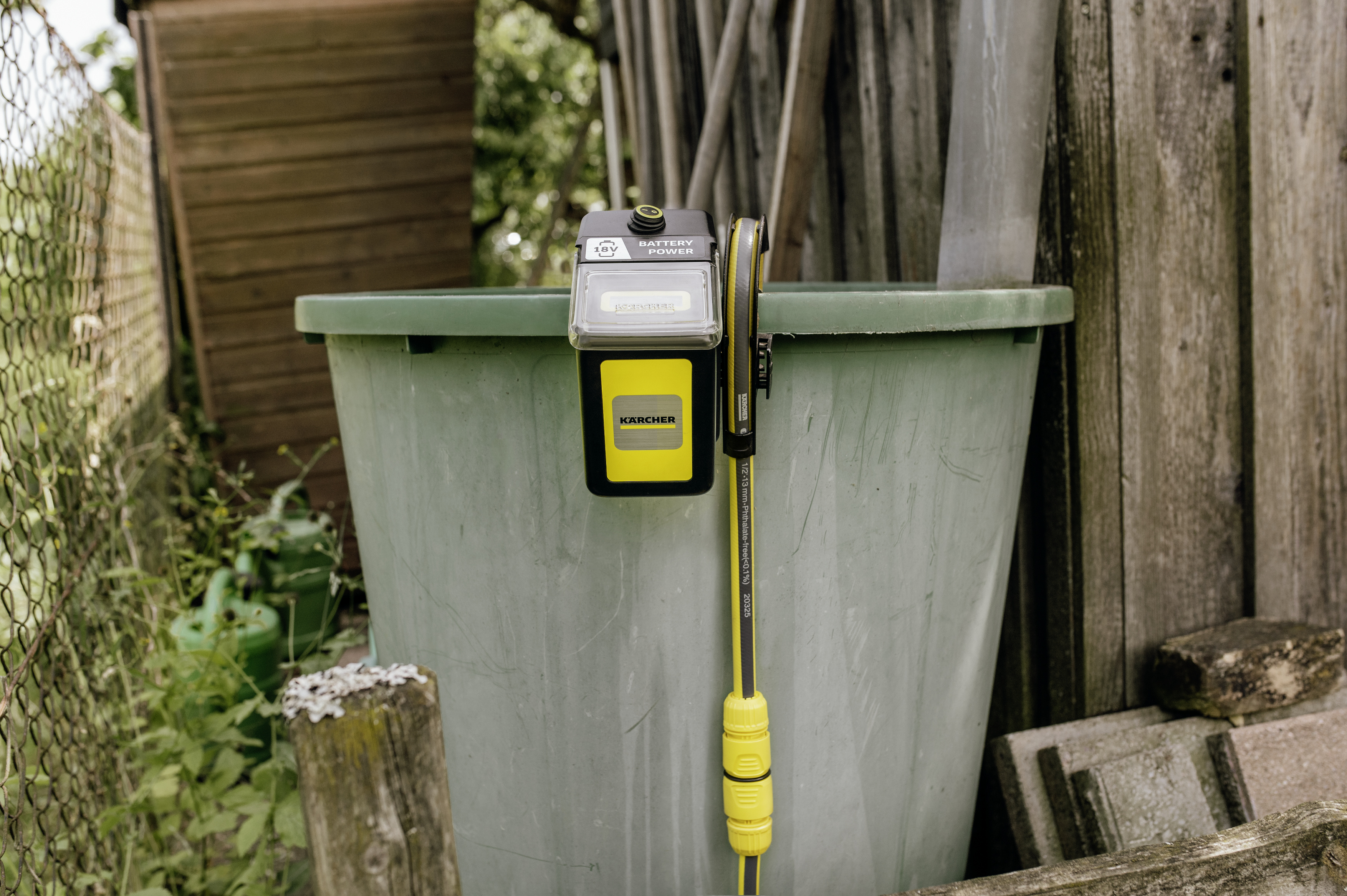 Un dispositivo de batería Karcher está sujeto al borde de un gran barril de lluvia verde.