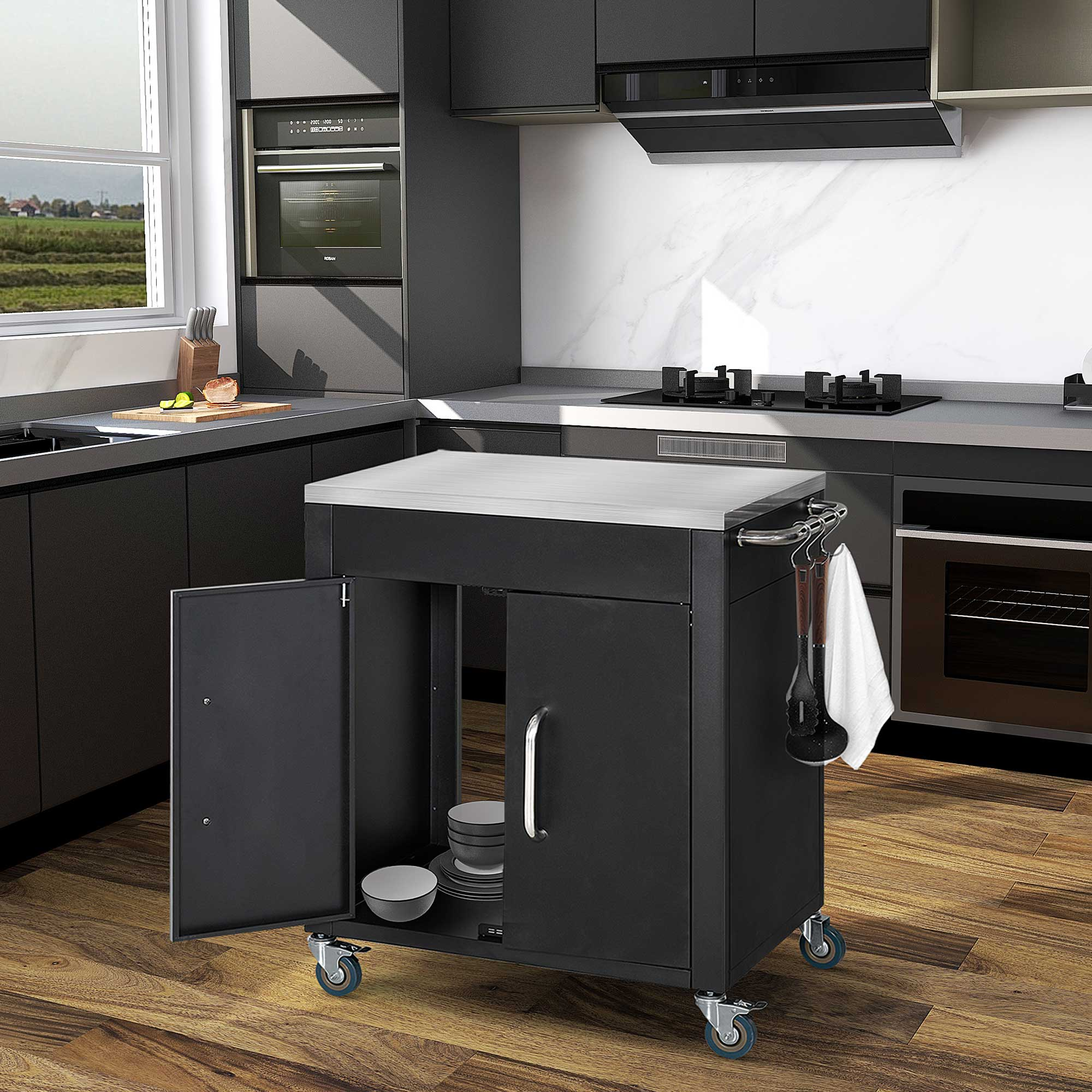 Carrello da cucina nero con piano in acciaio inox, ante aperte con piatti e ruote in una cucina moderna.