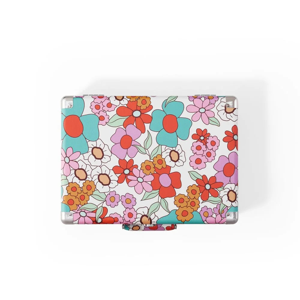 Ein kleiner Koffer mit buntem Retro-Blumenmuster in Rosa, Blau, Orange und Rot auf weißem Grund.