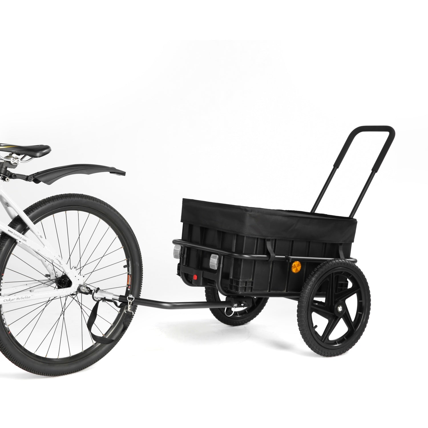 Un remolque de carga negro para bicicleta con una caja está sujeto al eje trasero de una bicicleta blanca sobre fondo blanco.