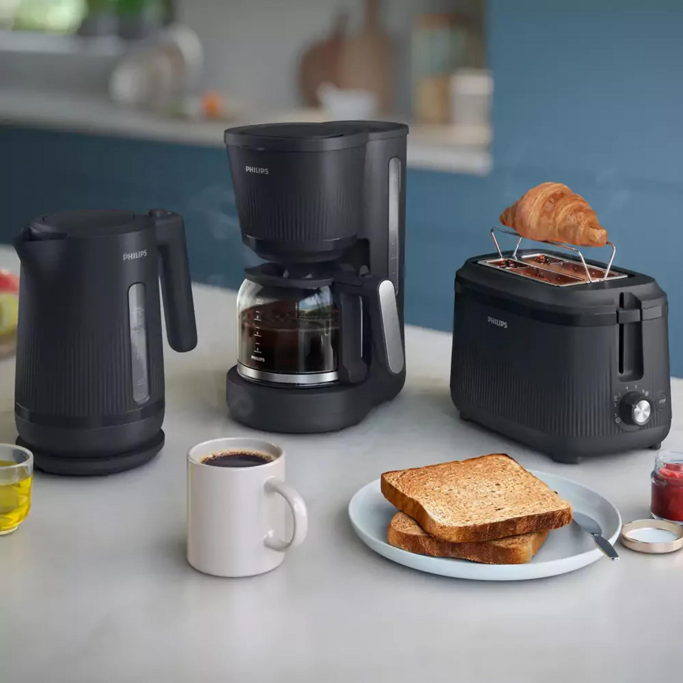 Set da cucina nero Philips con bollitore, caffettiera e tostapane con toast e croissant.