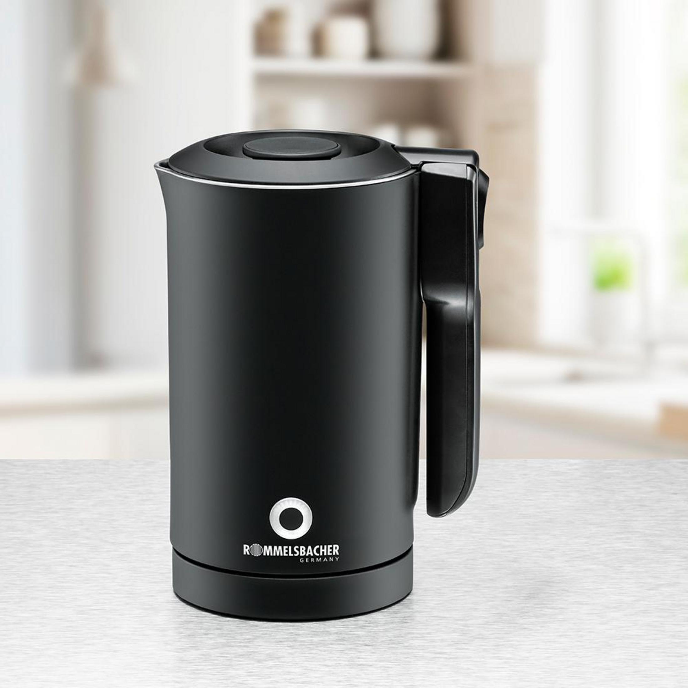 Un bollitore elettrico nero con manico integrato si trova su un piano di lavoro della cucina con sfondo sfocato.