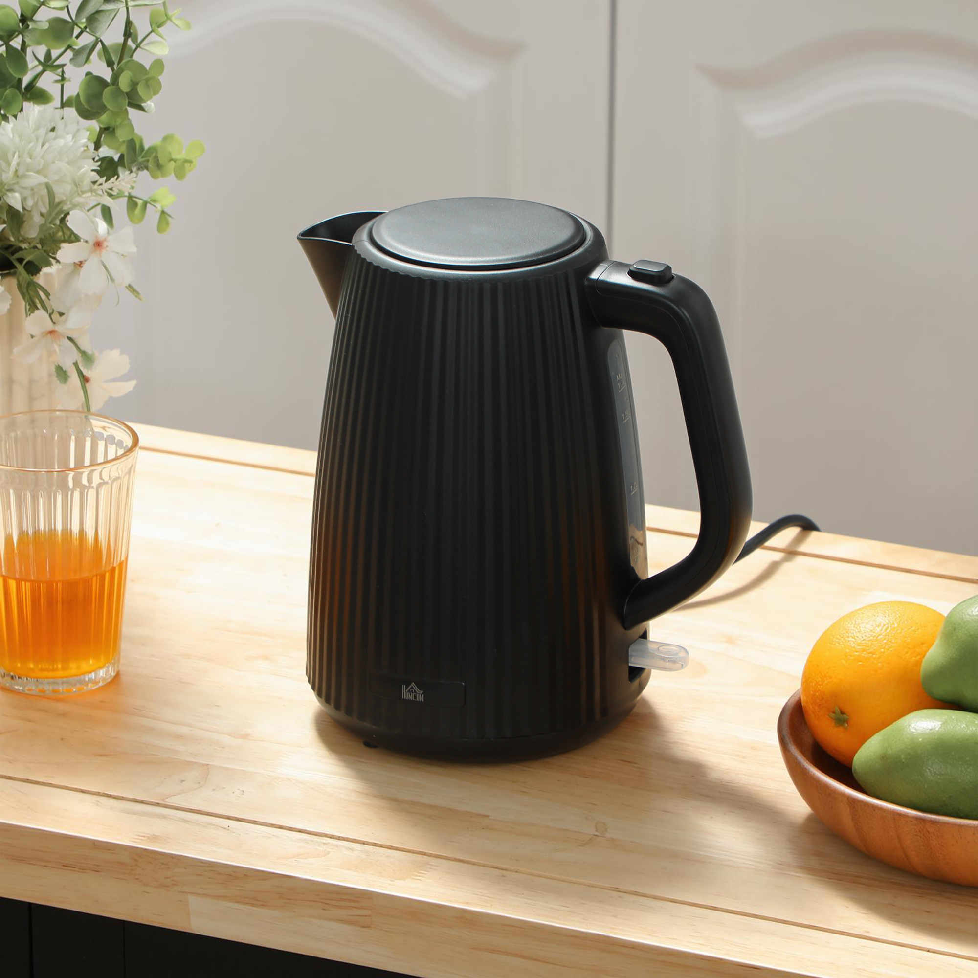 Un hervidor eléctrico negro acanalado se encuentra en una encimera de madera con jugo, fruta y flores.