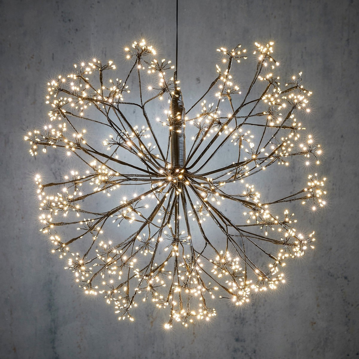 A spherical, starburst-style chandelier with numerous tiny lights on delicate branches against a grey wall.