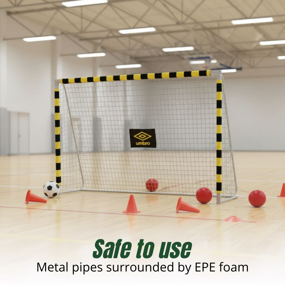 Indoor handball goal with yellow and black padding, soccer ball, red balls, and cones on a wooden floor.
