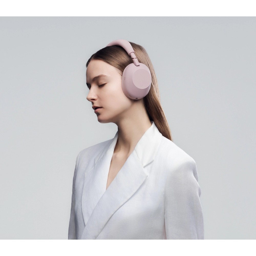 Una donna in giacca bianca con gli occhi chiusi indossa cuffie rosa.