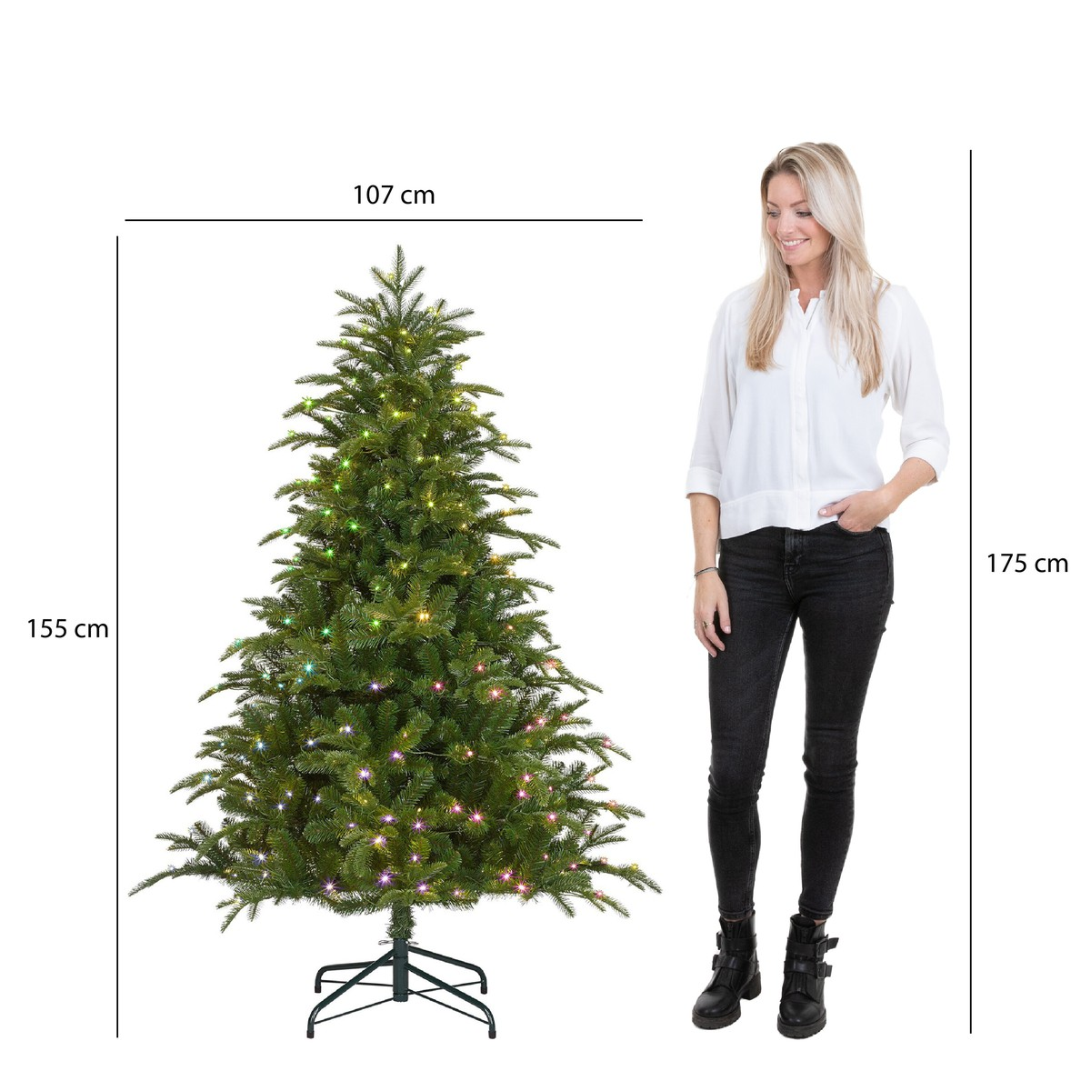 A woman in a white shirt and black jeans stands next to a 155 cm Christmas tree with lights.