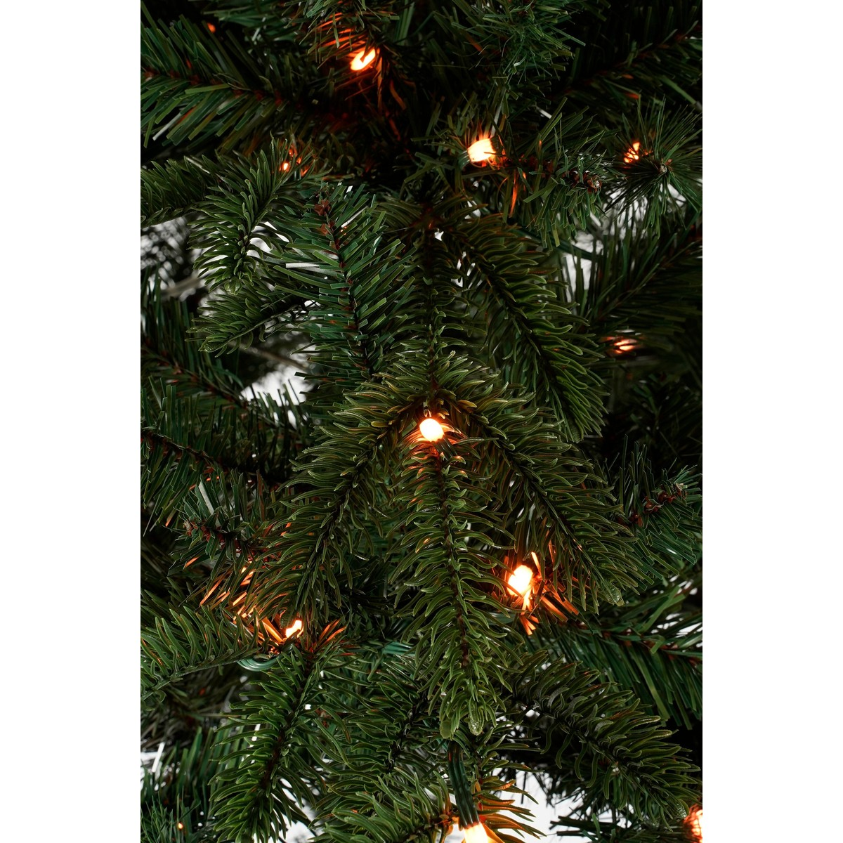Green artificial Christmas tree branches adorned with warm, glowing lights.