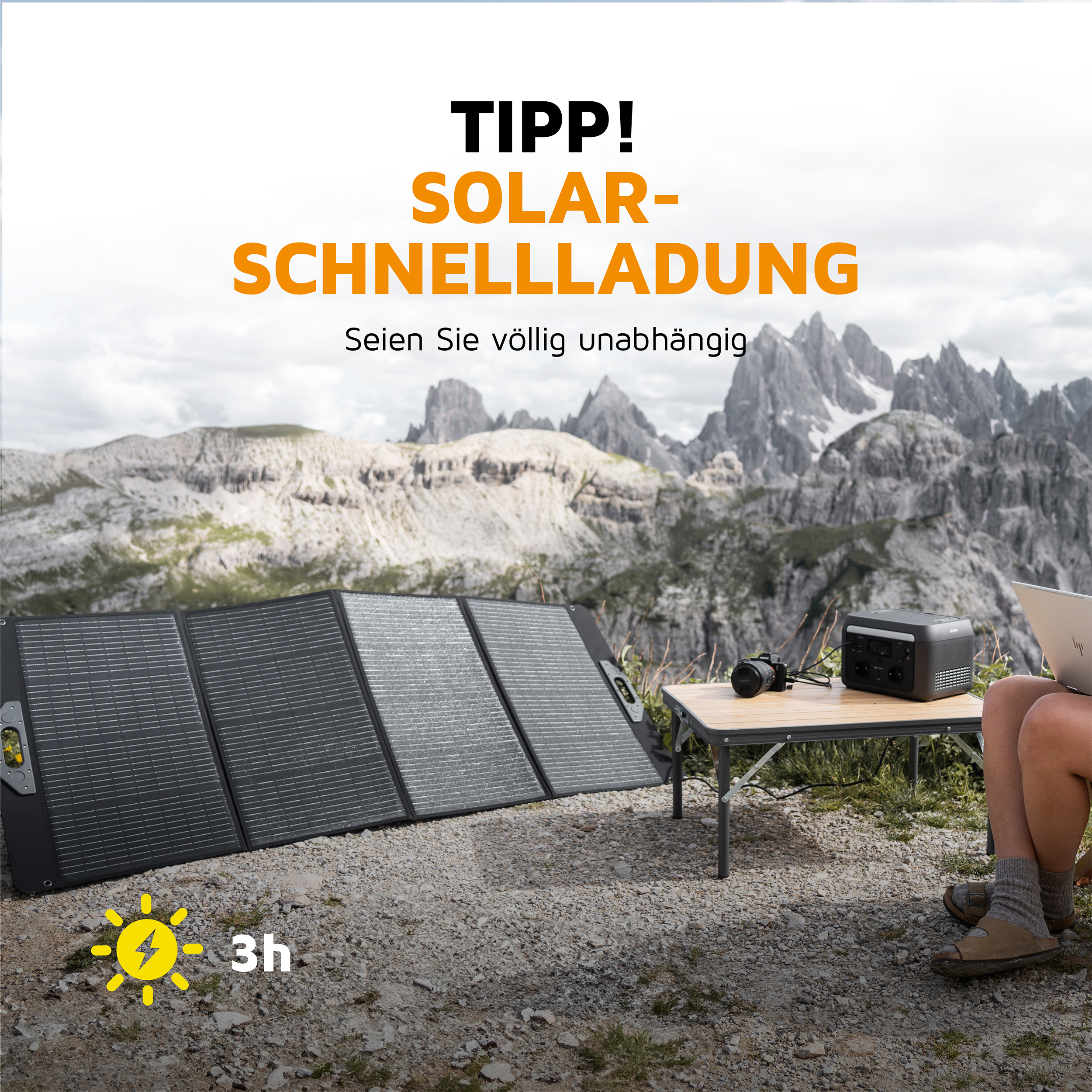 Tragbares Solarpanel und Kraftwerk auf einer Bergwiese, Person sitzt mit Laptop.